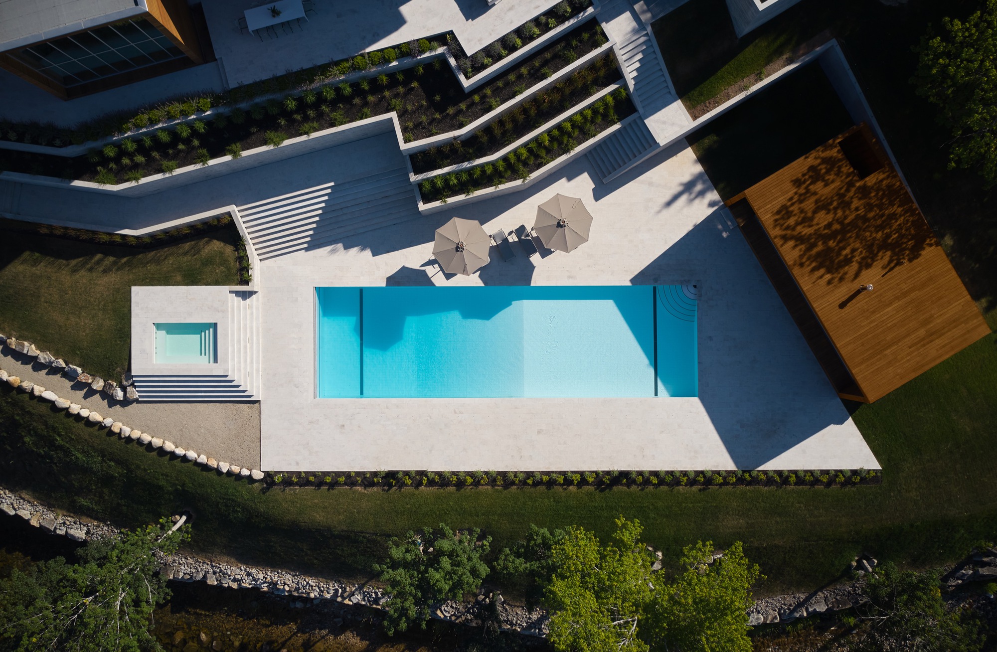 Overhead view of the pool terrace with lounge seating and planted retaining walls descending to the shoreline