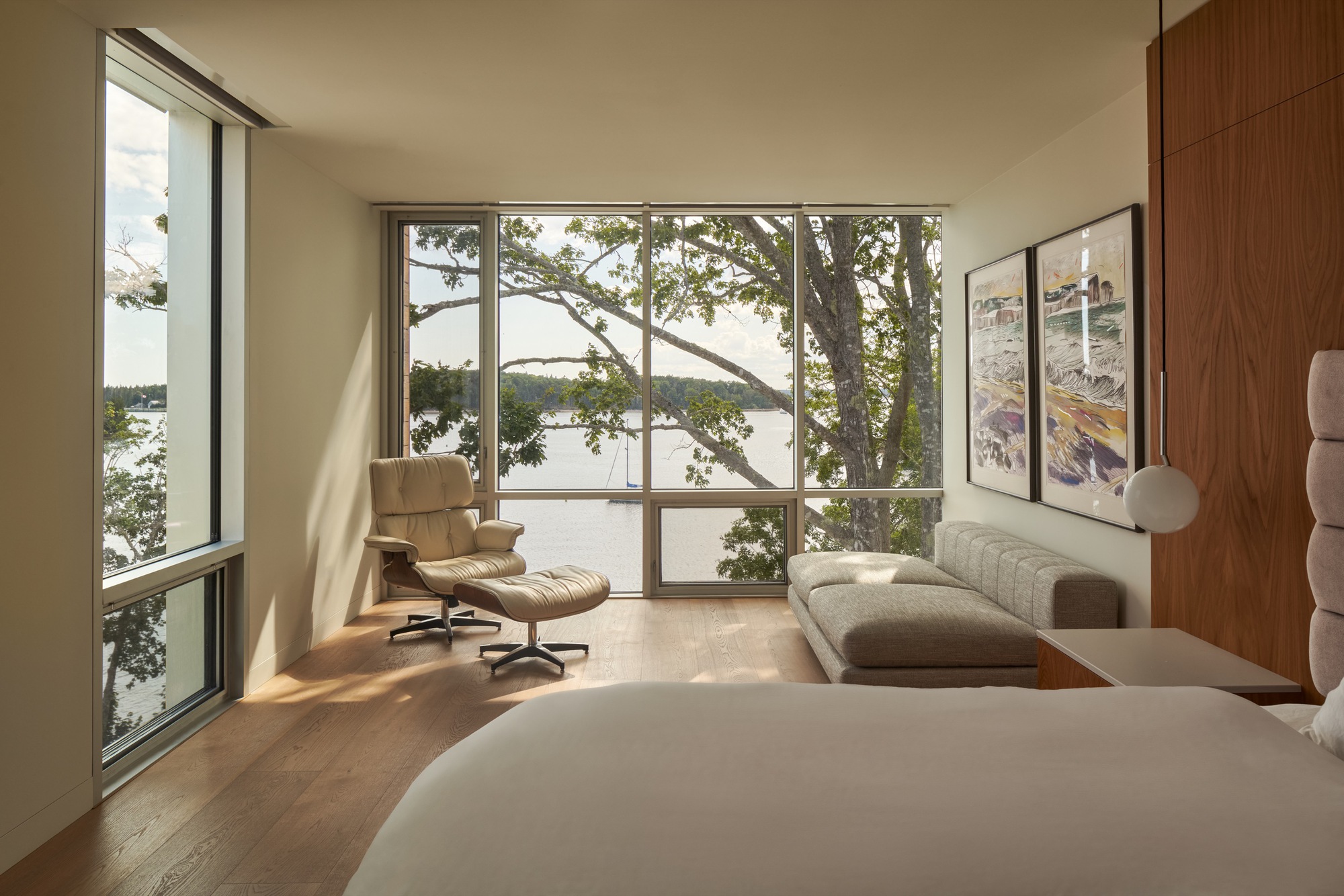 Corner bedroom with floor-to-ceiling glazing framing tree branches and water beyond