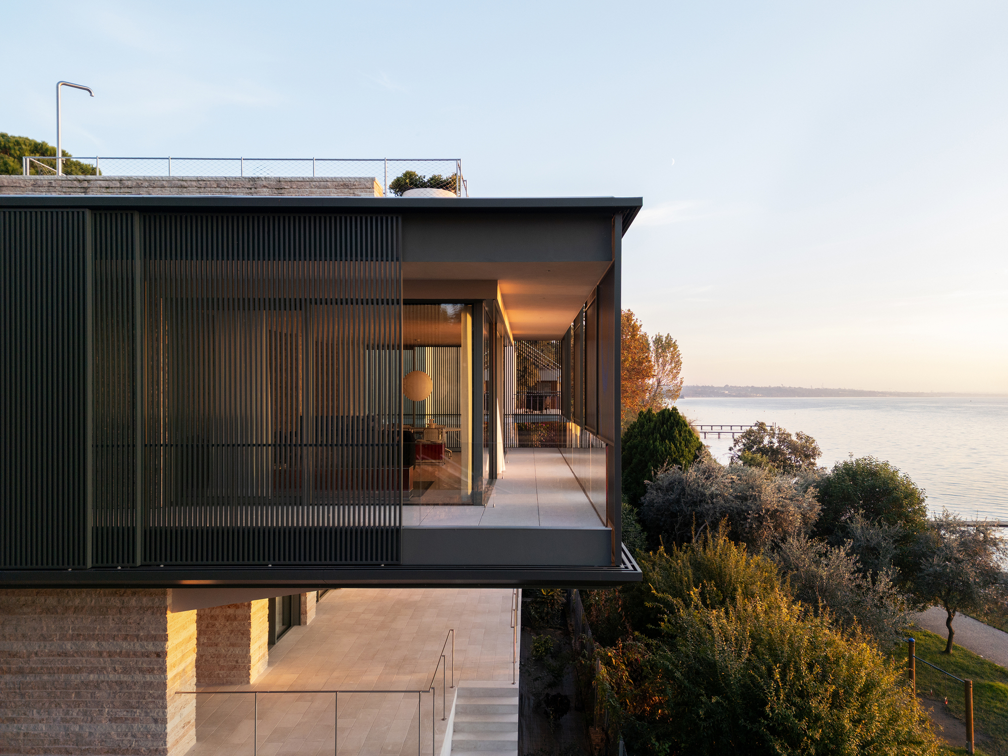 Cantilevered upper volume with vertical metal cladding and recessed glazing overlooking the water at dusk