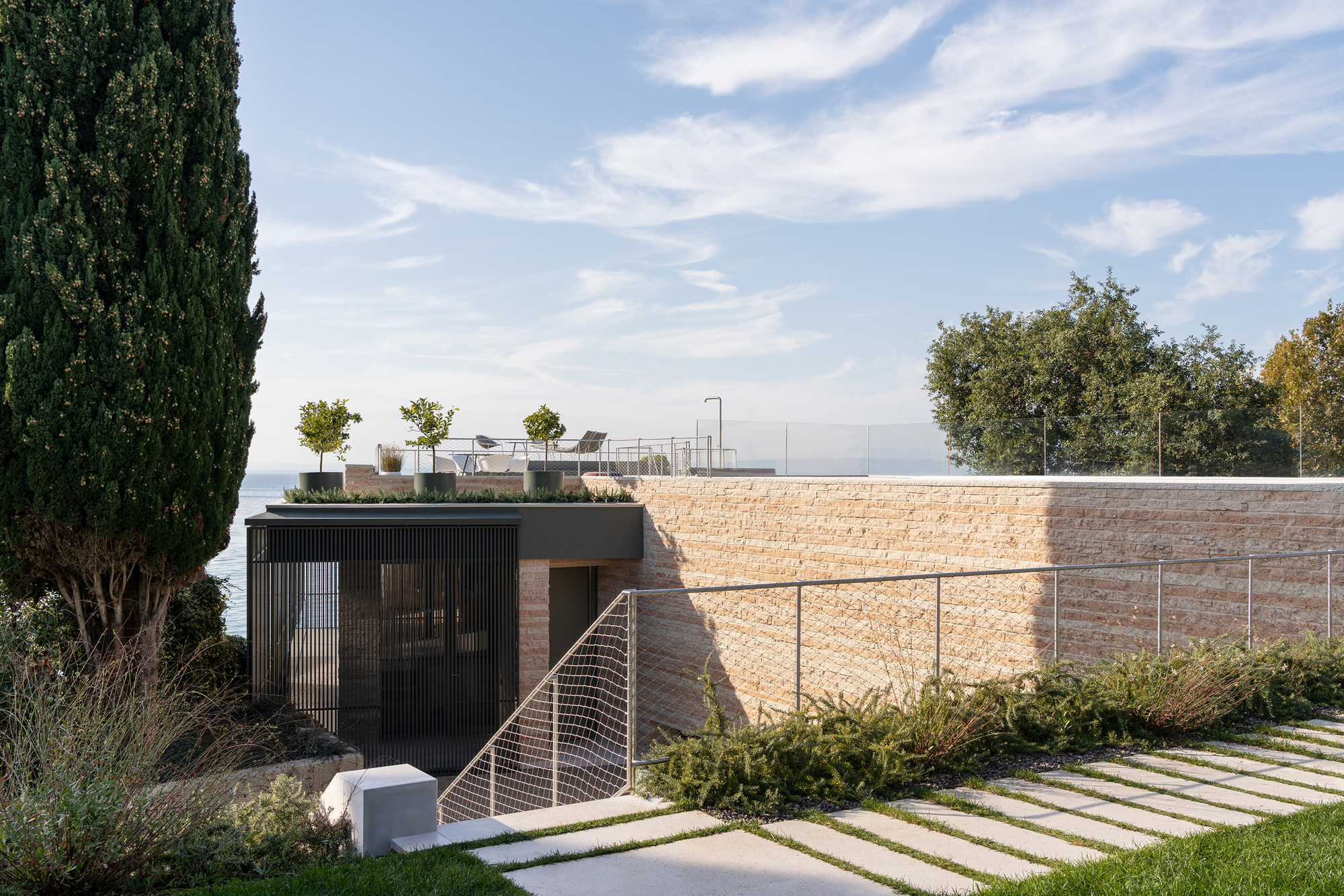 Planted roof terrace above rammed earth retaining wall with stepping stone path and cypress