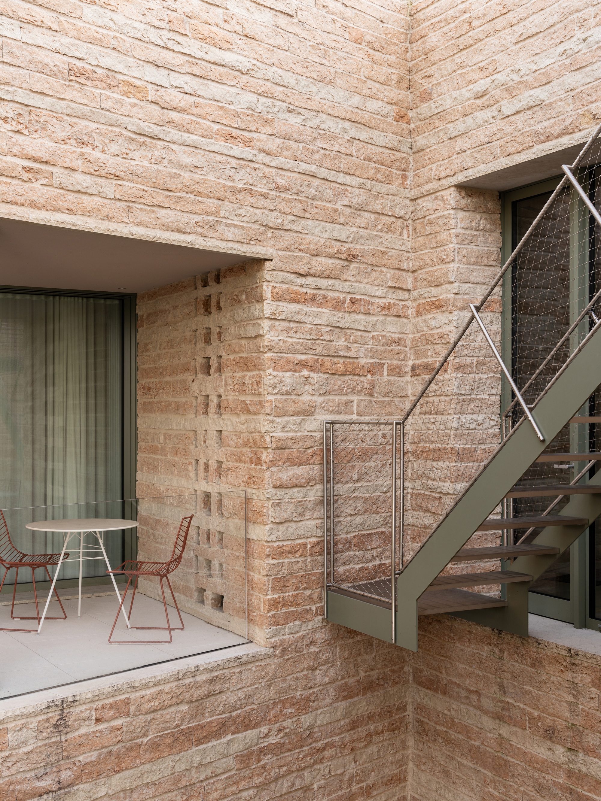 Courtyard corner with layered stone walls, a metal staircase, and a table set beneath a recessed balcony