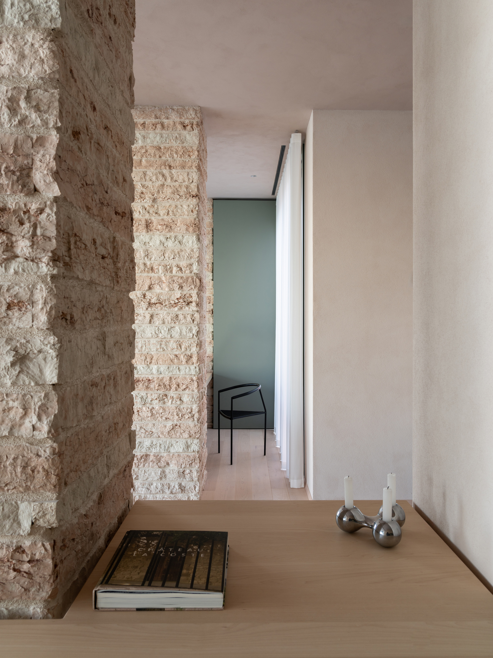 Hallway threshold between rough stone wall and smooth white plaster with a doorway visible beyond