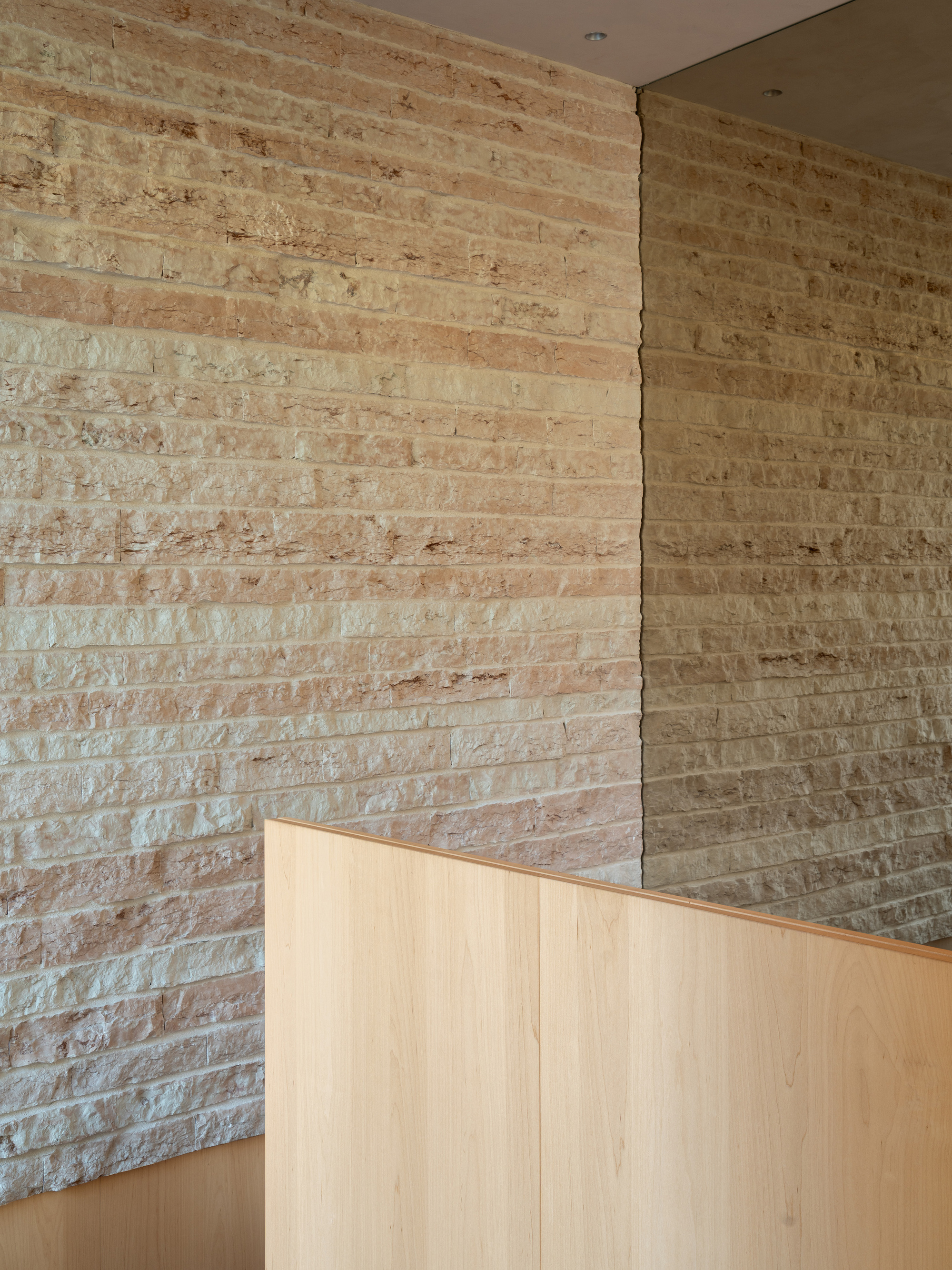 Corner detail of layered stone masonry meeting a pale wood cabinet under a ceiling recess