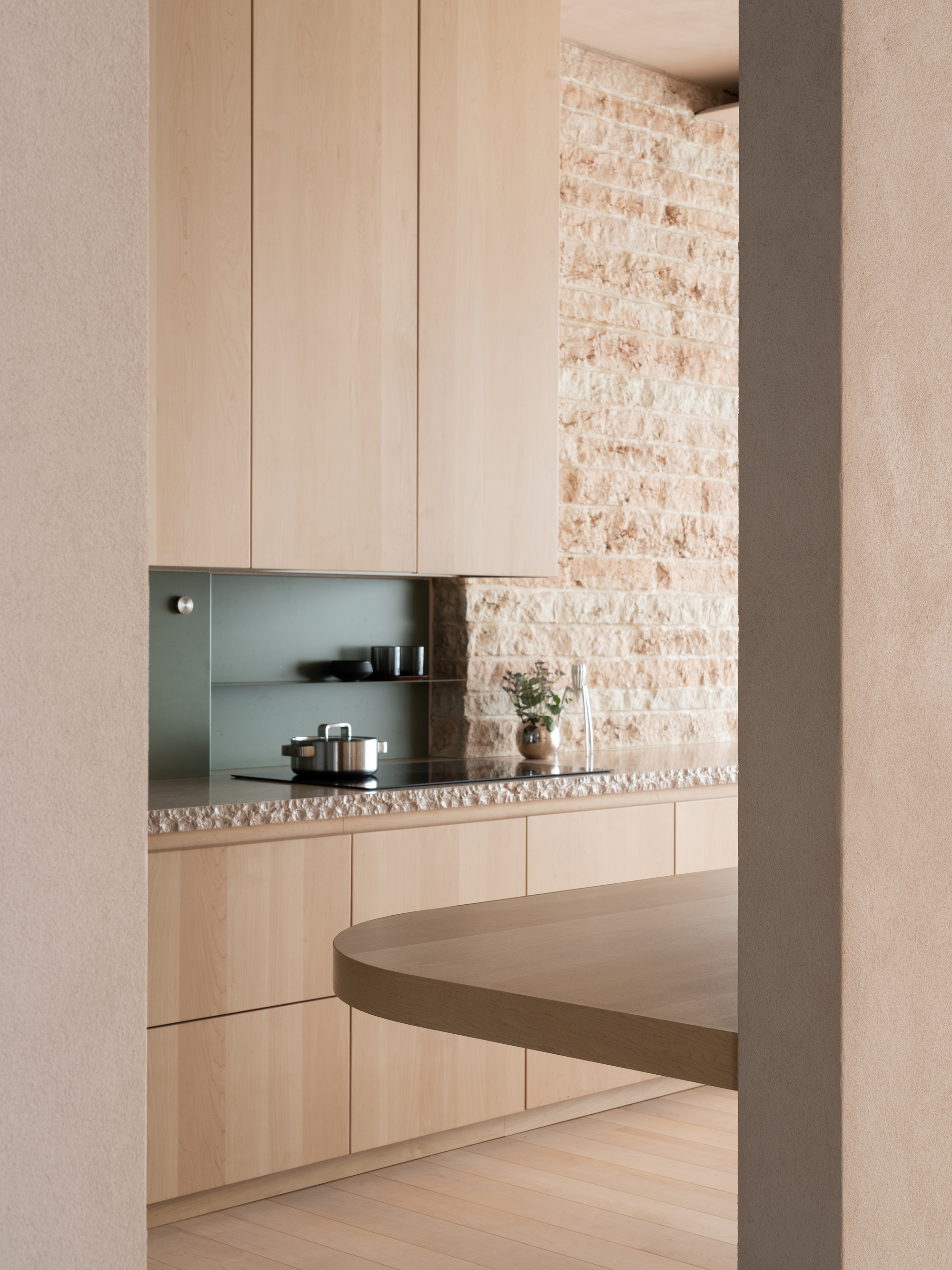 View through doorway into kitchen with pale timber cabinetry, terrazzo counter and exposed brick wall