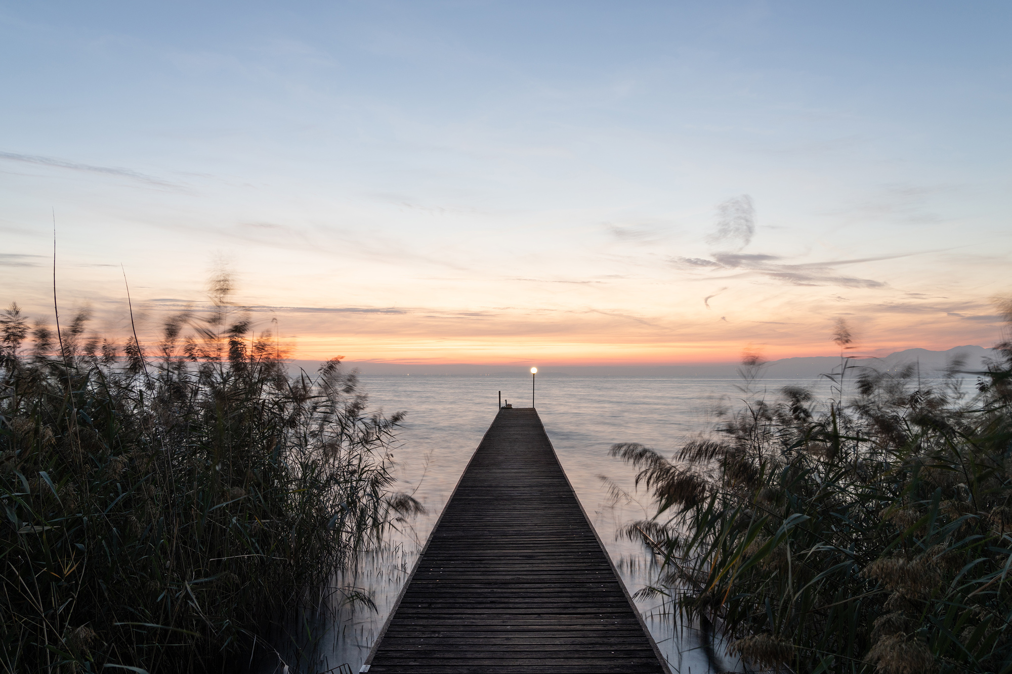 Timber boardwalk extending through reeds toward the lake at sunset