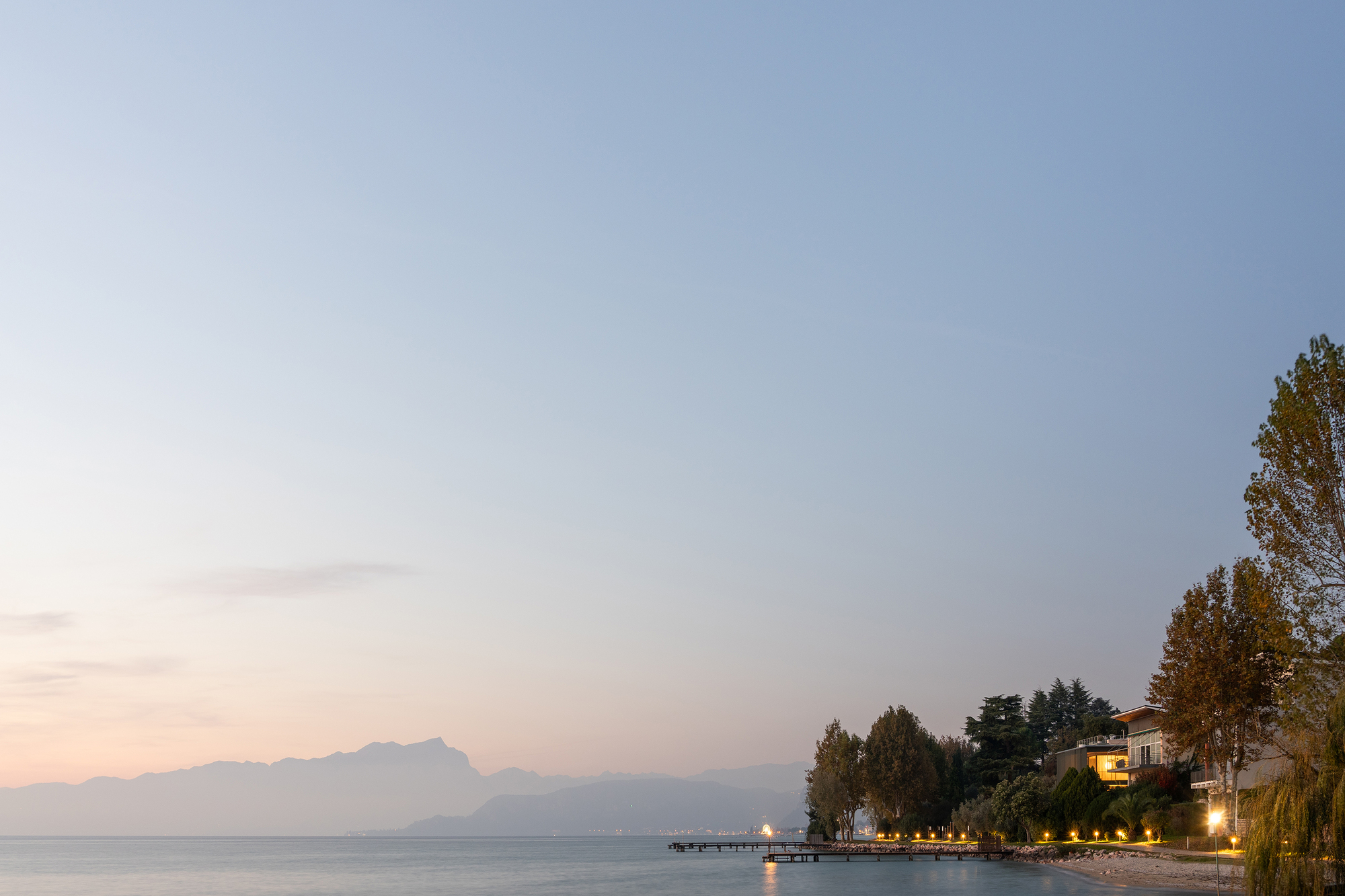 Lakefront property with illuminated windows and exterior path lights among trees in the evening