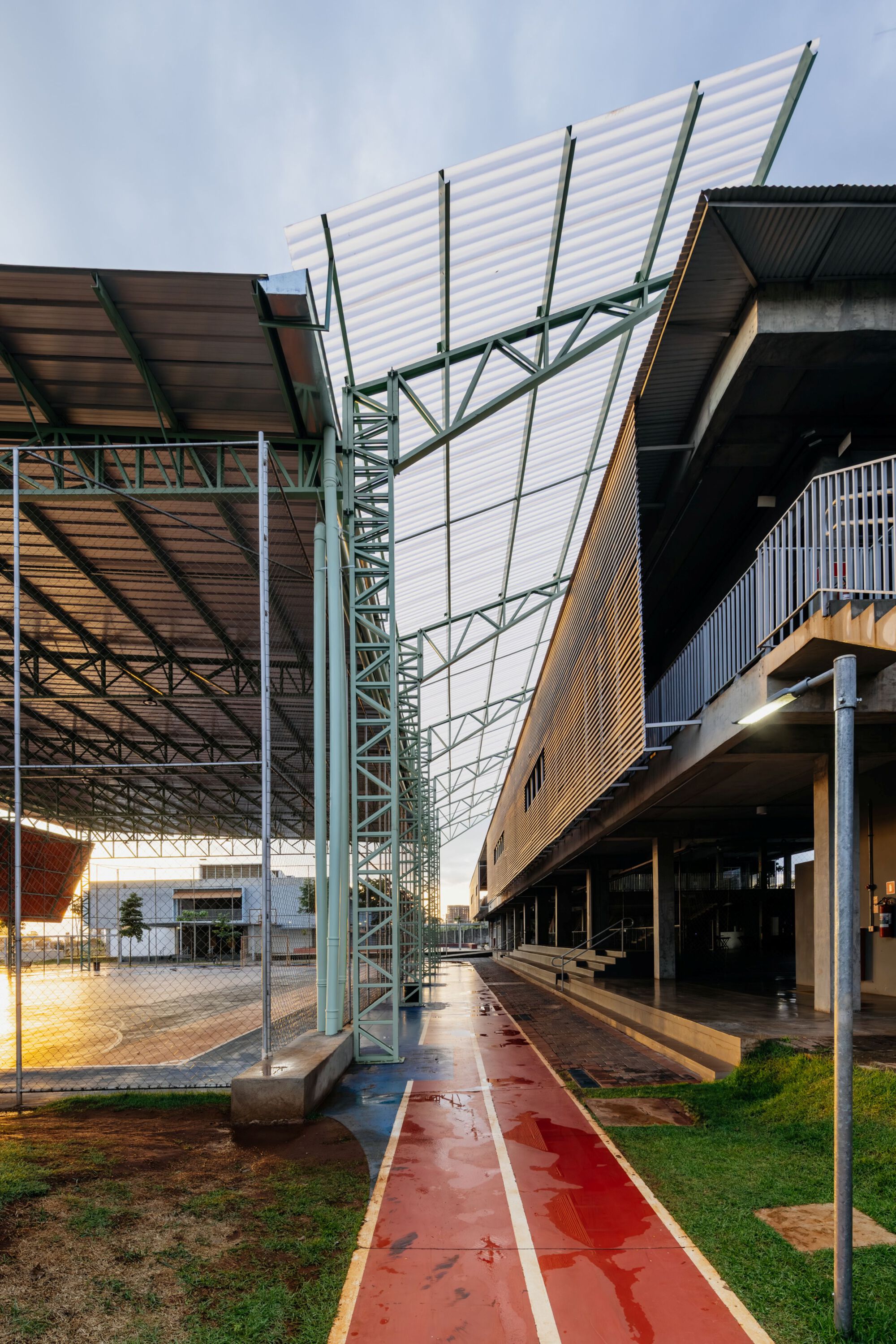 View along the covered walkway showing the angled white corrugated canopy supported by green steel trusses