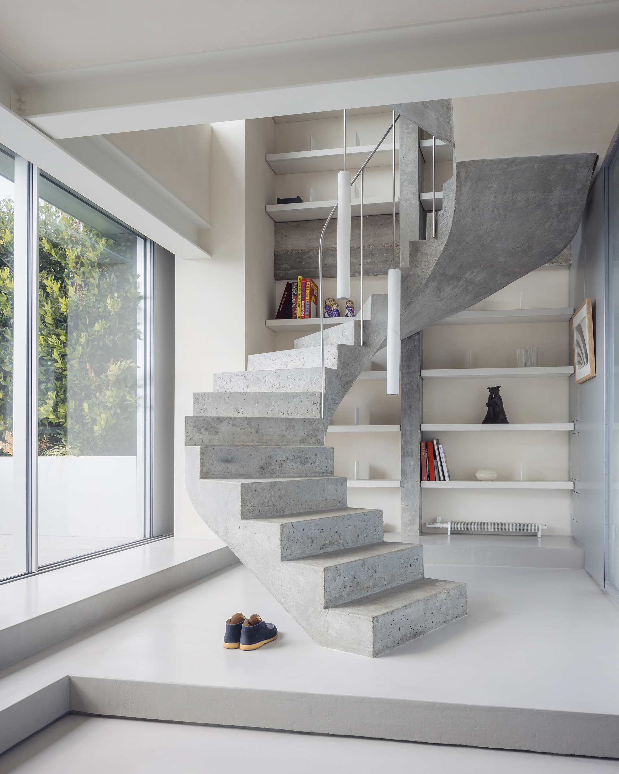 Concrete staircase with cantilevered treads and metal railing beside floor-to-ceiling glazing and built-in shelves
