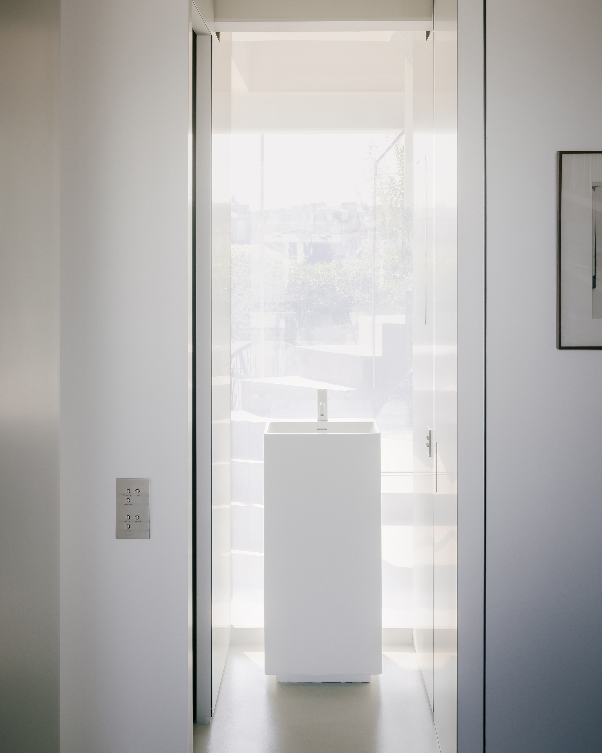 Narrow corridor with white pedestal sink framed by doorway under diffused natural light