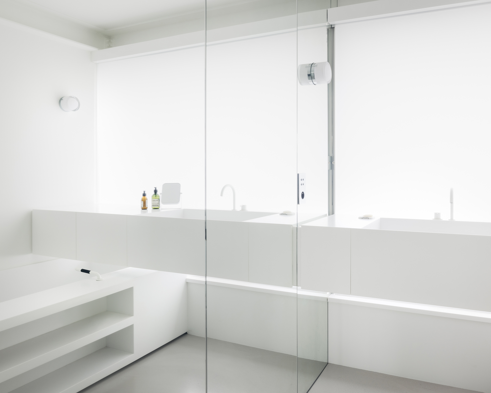 Bathroom vanity with glass shower partition and continuous horizontal mirror under recessed lighting