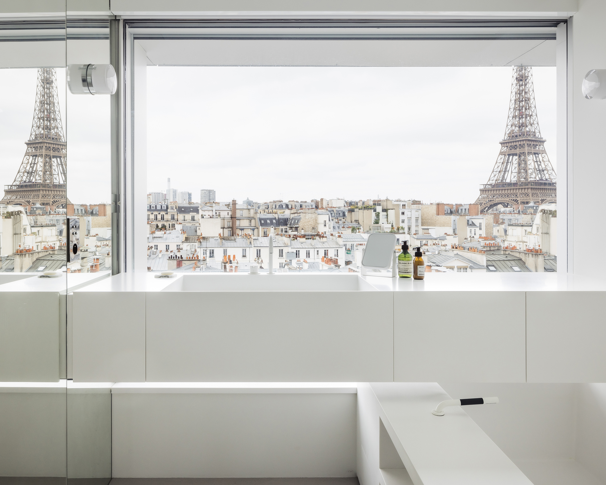 Bathtub edge and window opening framing rooftops and tower beyond under overcast sky