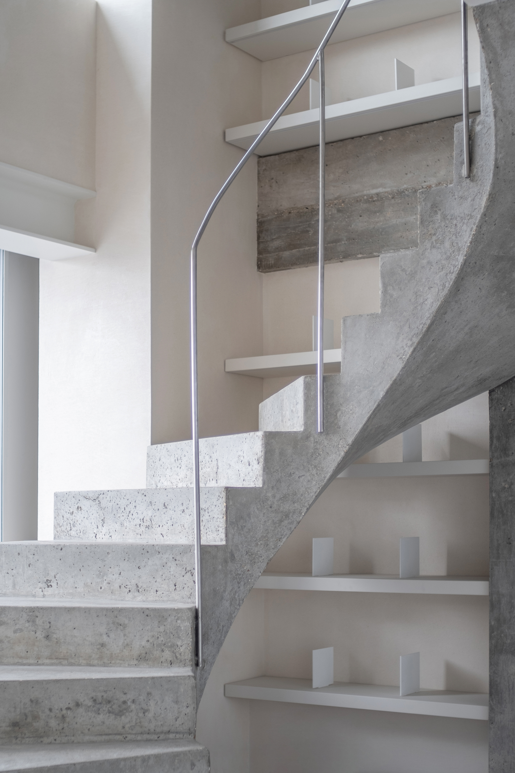 Concrete and metal staircase with curved handrail ascending through double-height space