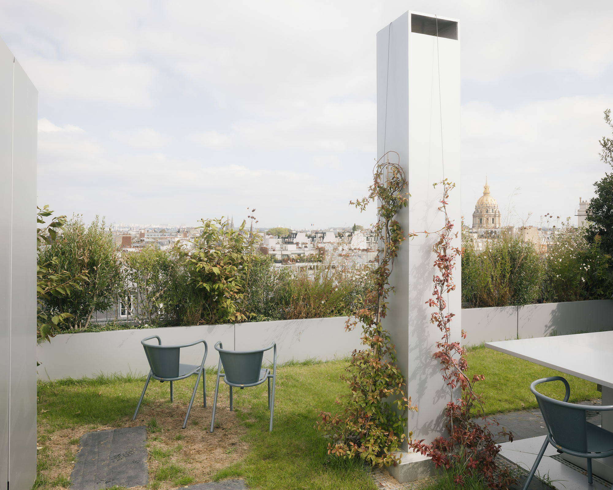 Rooftop garden with two green chairs and planted beds overlooking the urban skyline under overcast skies
