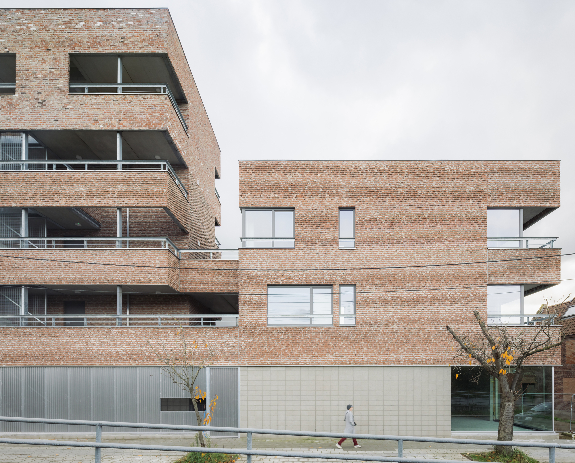 Brick facade with offset windows and recessed balconies along a planted sidewalk