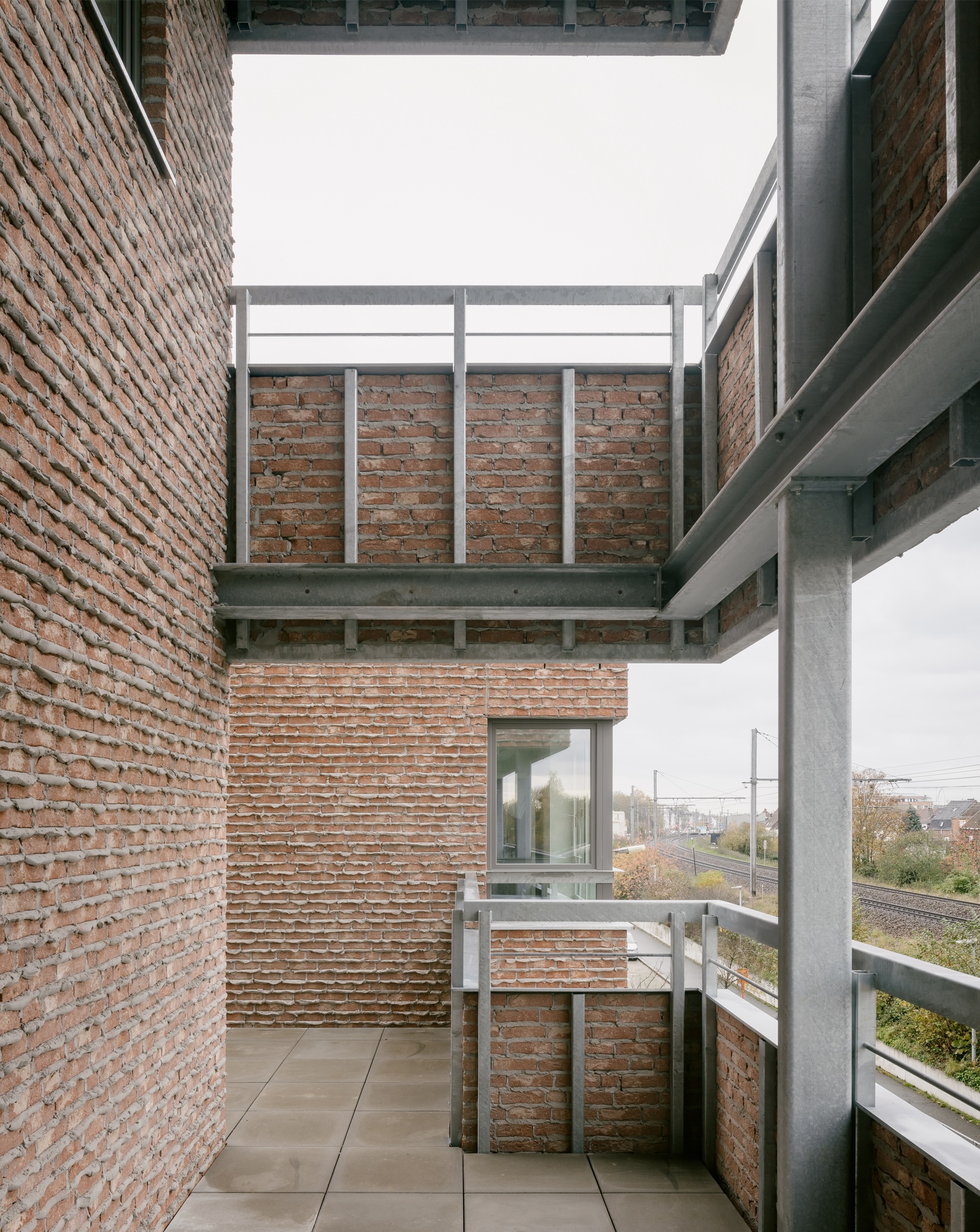 Concrete balcony framed by brick walls with metal railings overlooking rail tracks