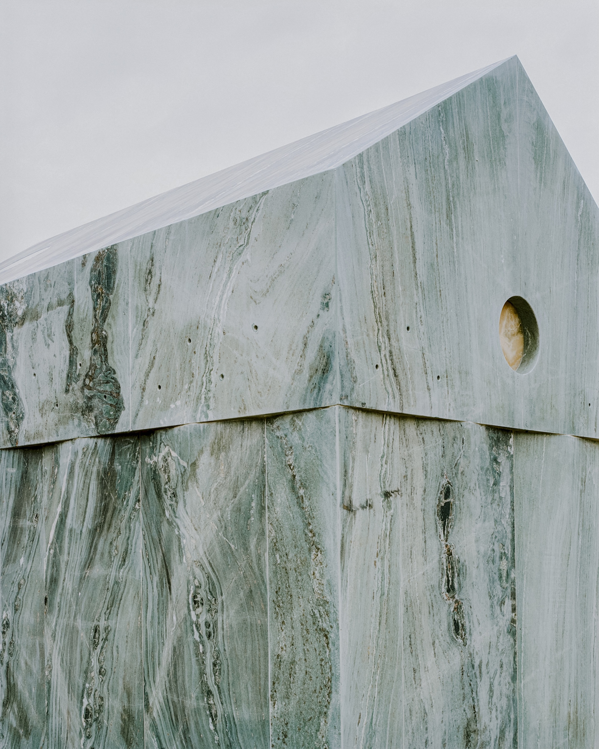 Detail of the upper corner where marble panels meet at the gable edge with circular oculus