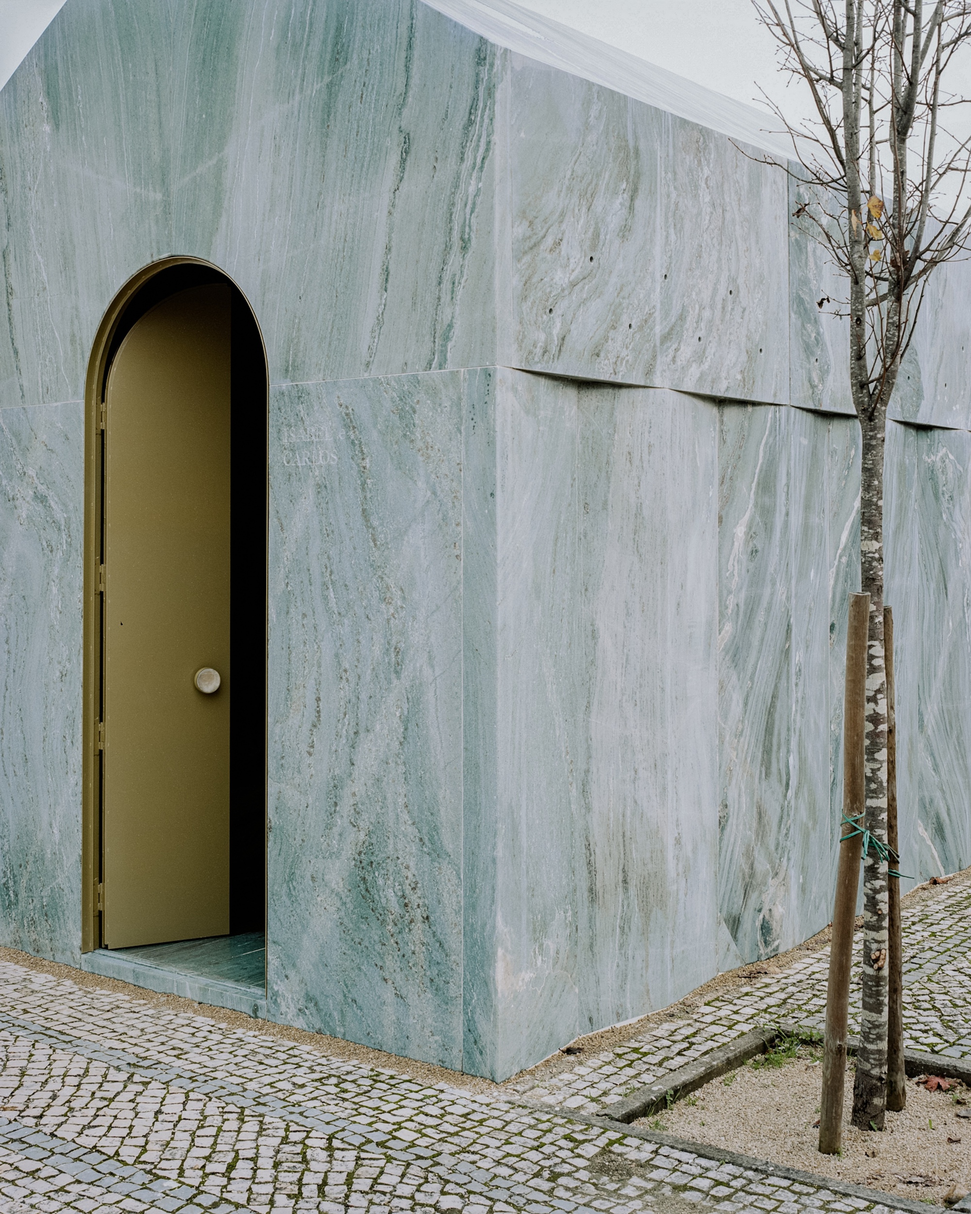 Corner detail of the veined marble facade with arched brass door and horizontal panel joints