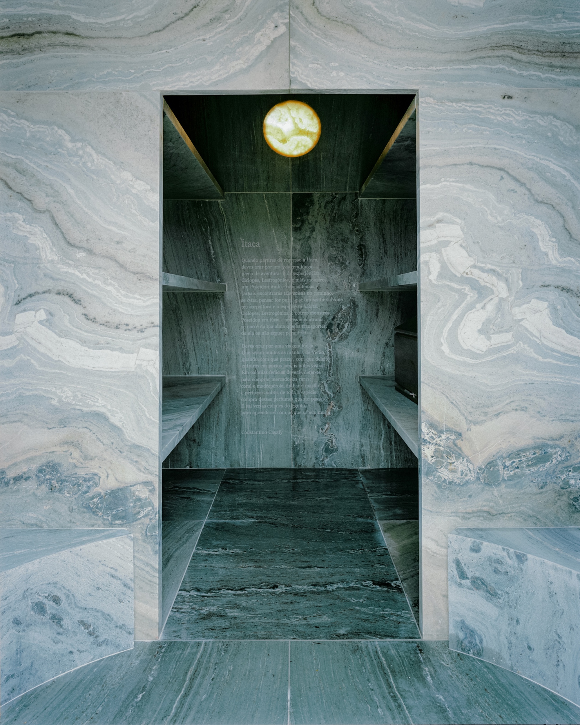 View through a doorway into a vaulted interior lined with veined grey marble and a suspended circular light fixture