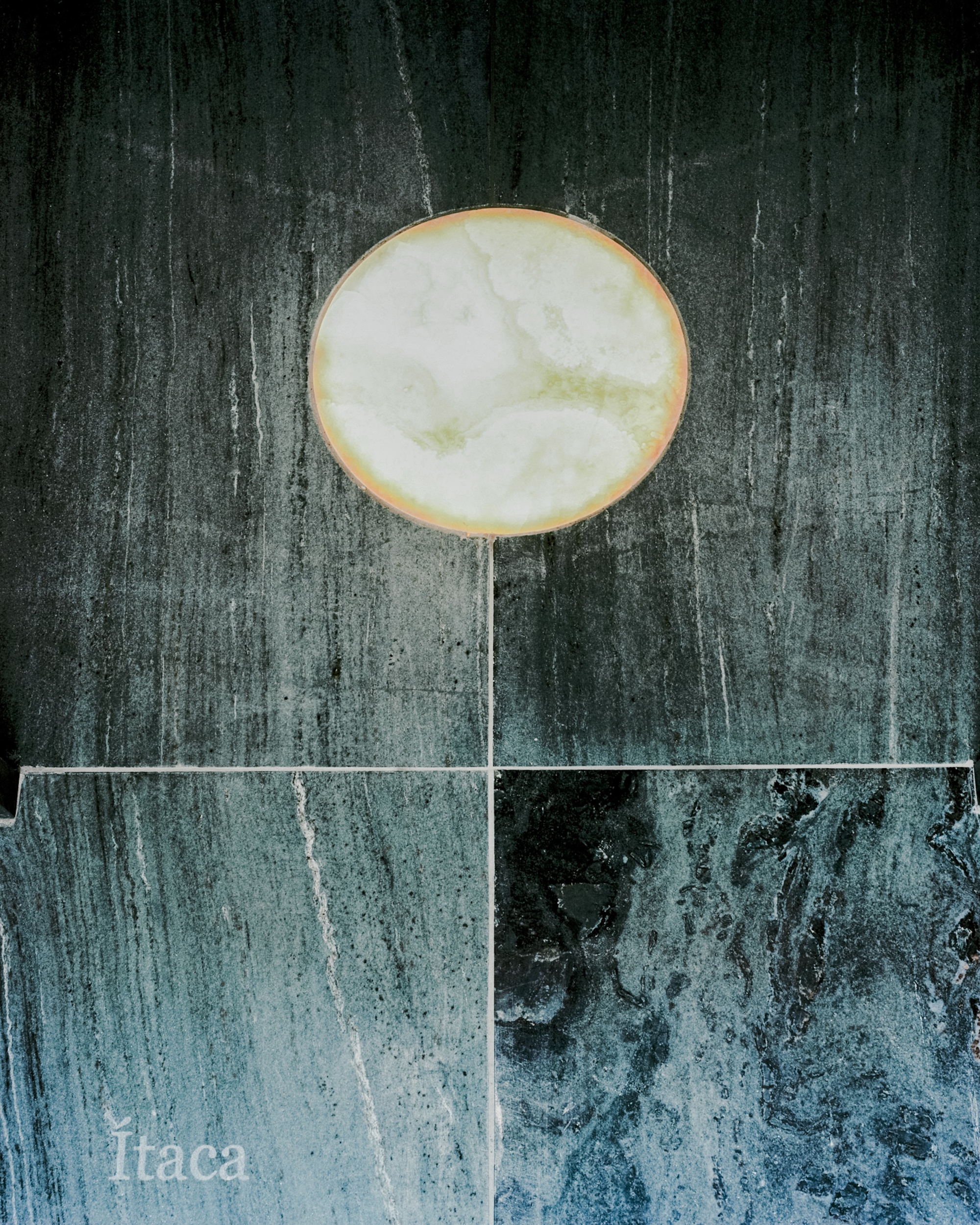 Detail of a backlit translucent stone disc with brass edging against dark veined marble wall panels