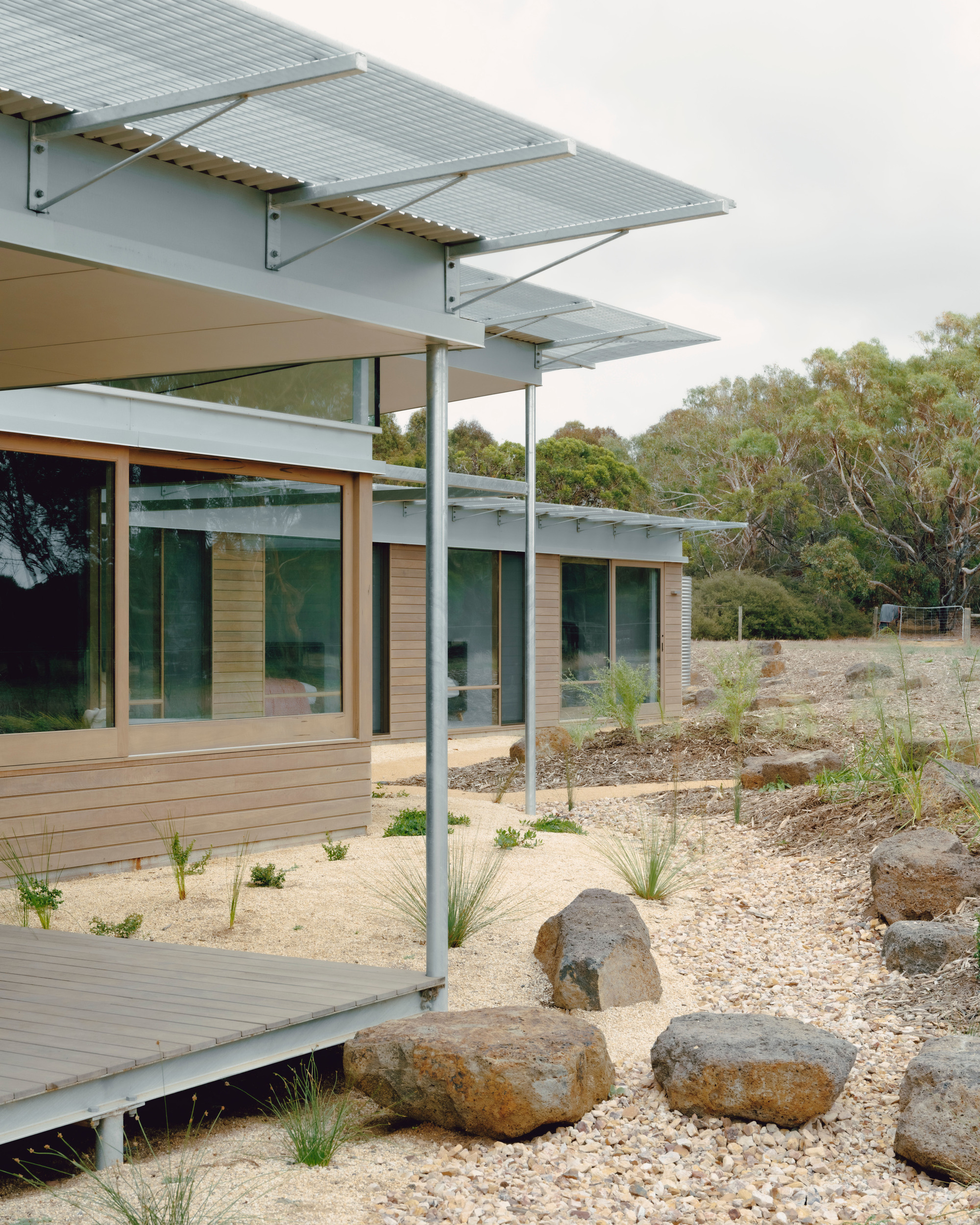Exterior deck with perforated metal canopy supported by slender steel columns above a gravel garden