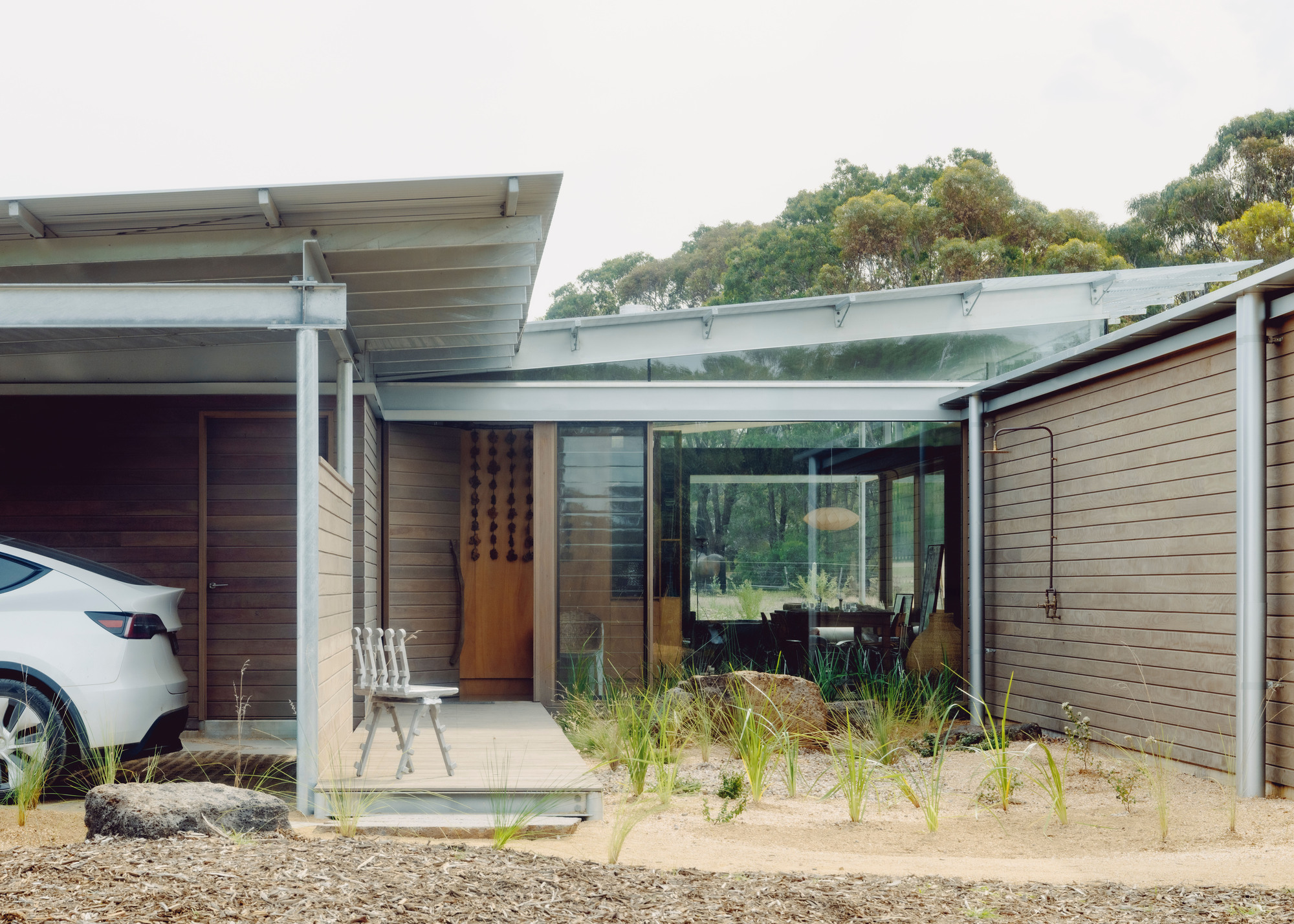 Entry courtyard with timber cladding and translucent canopy framing glass-walled living spaces