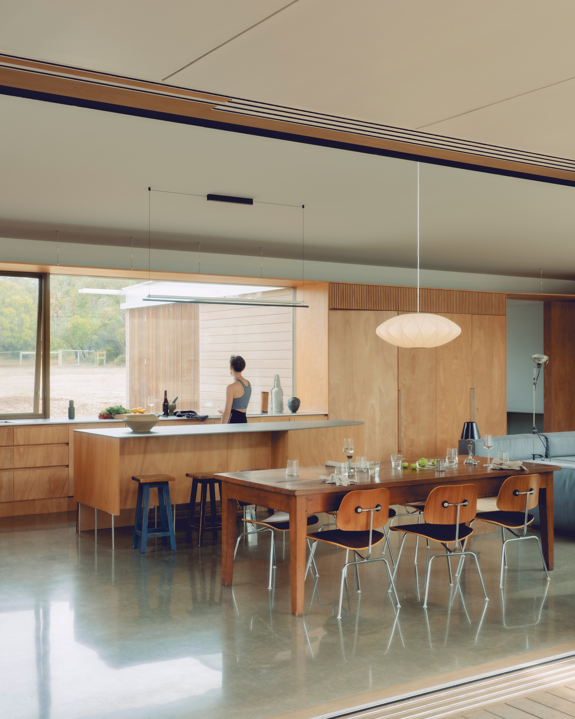 Open kitchen and dining area with timber cabinetry and polished concrete floor where a person prepares food