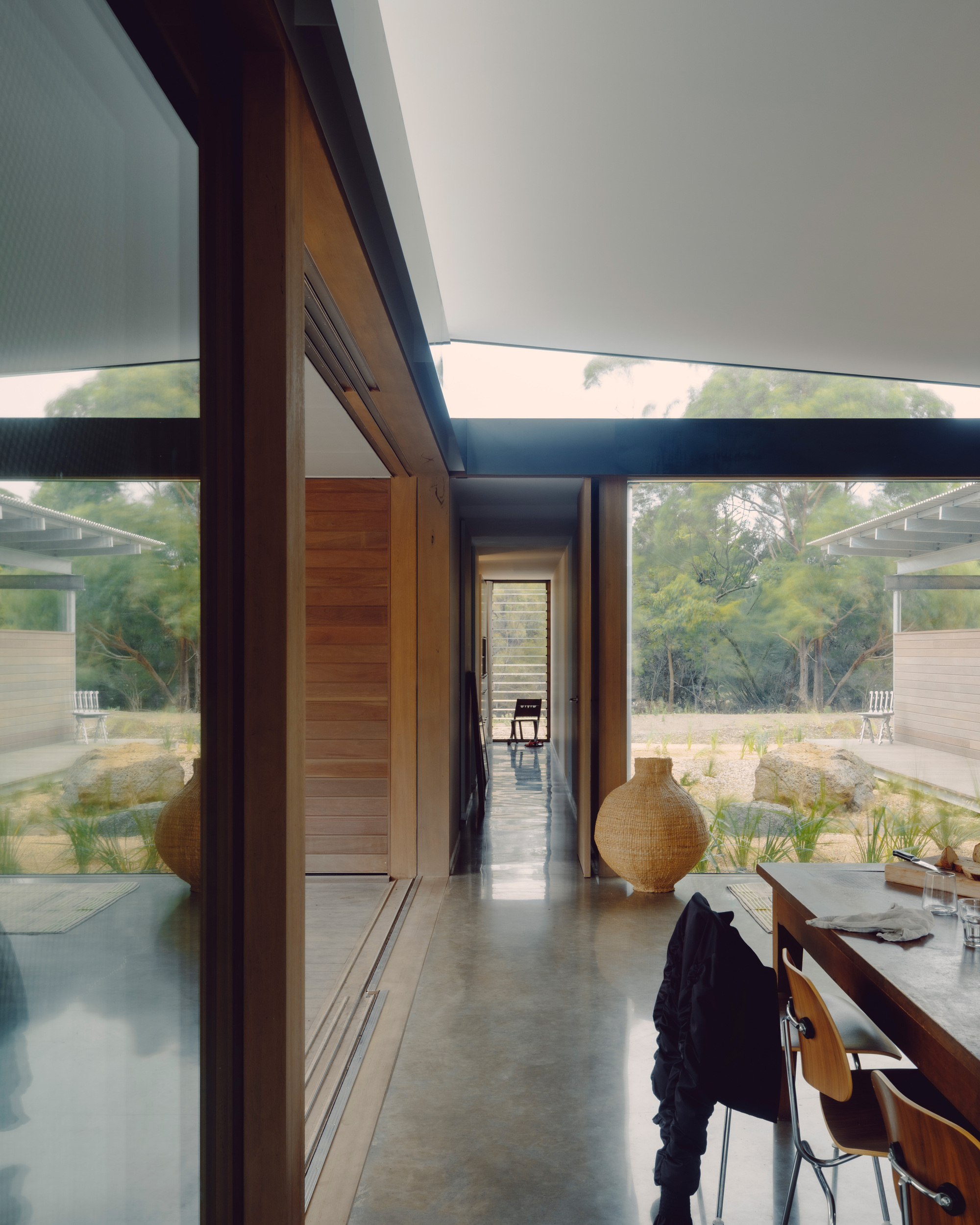 Interior corridor with timber-lined walls and clerestory windows opening to a courtyard with native grasses