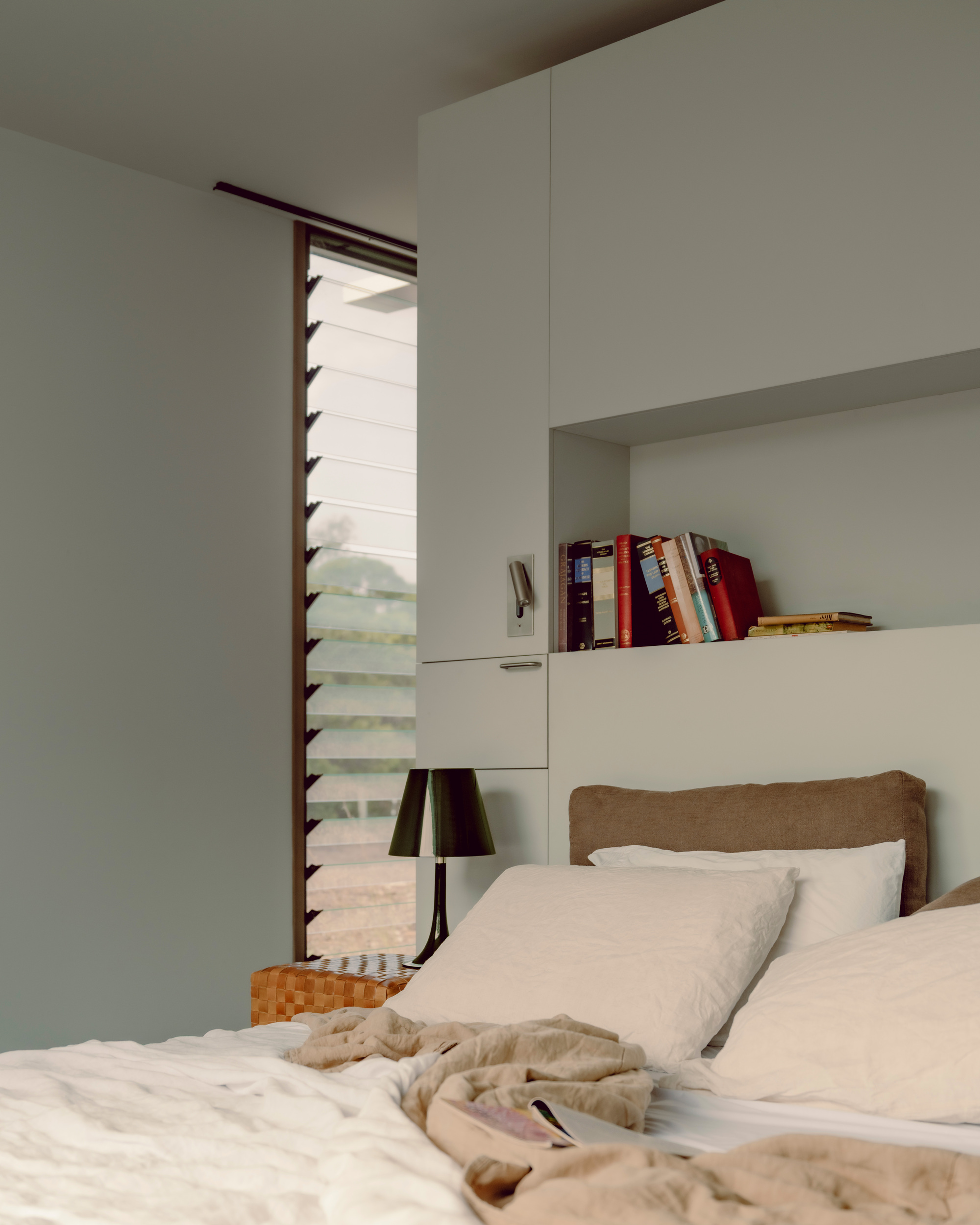 Bedroom with recessed shelving and louvered window opening to filtered daylight