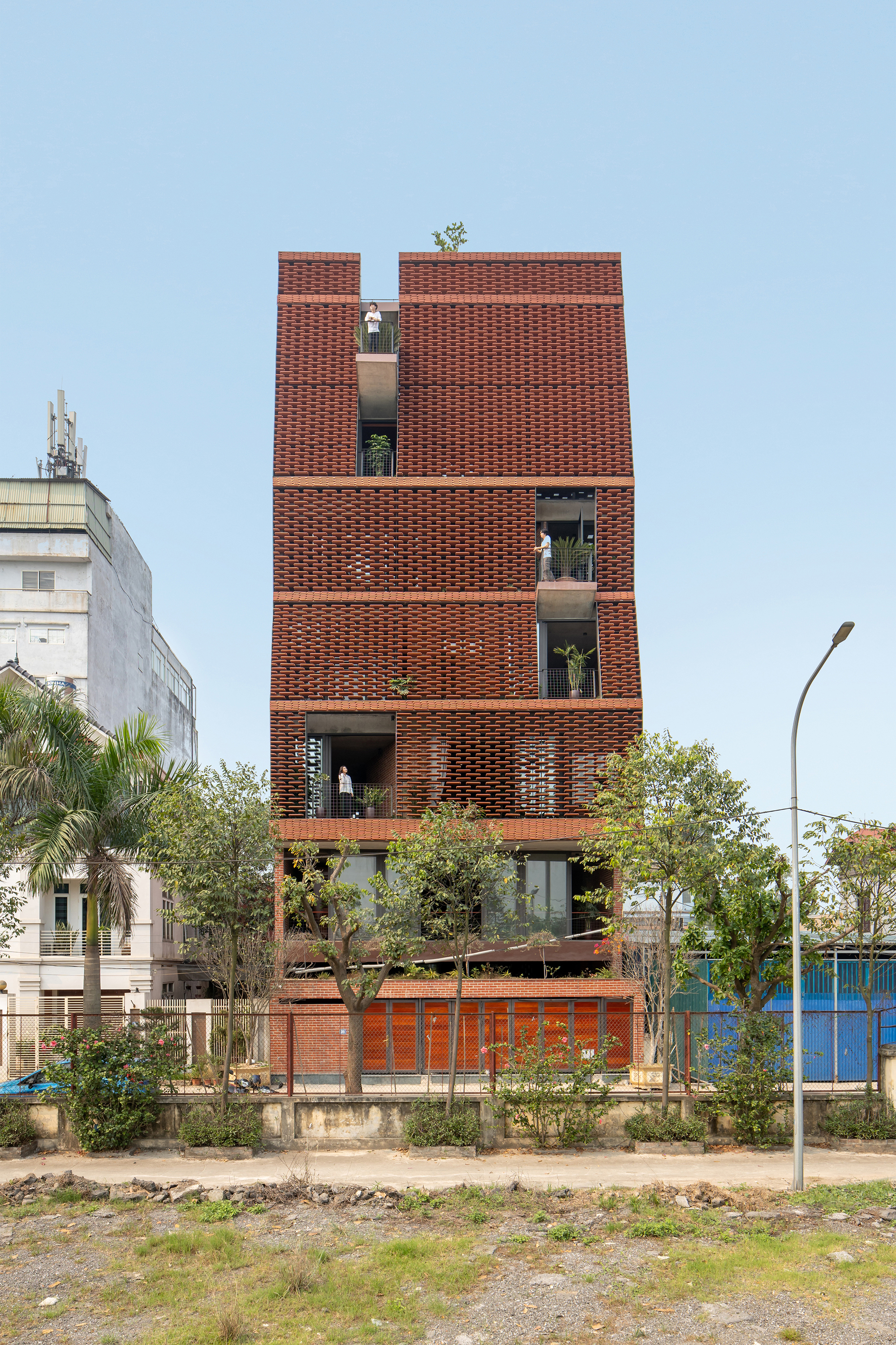Street view of the patterned brick facade with recessed balconies and young trees in the foreground
