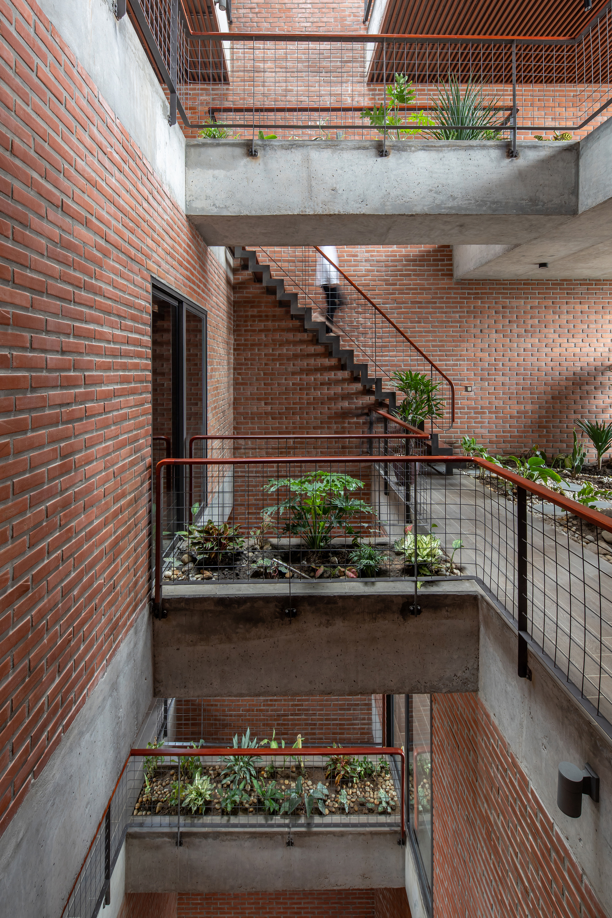 Interior atrium with concrete landings, planted boxes, and brick walls ascending to a skylight above