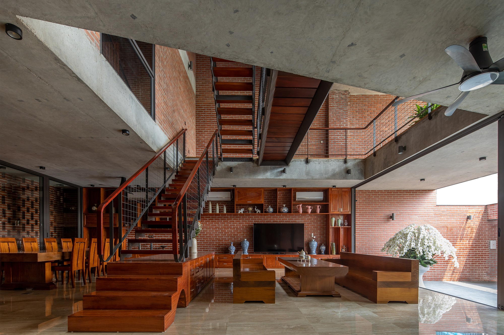 Multi-level living space with timber stairs, wire mesh railings, and exposed concrete ceilings under natural light