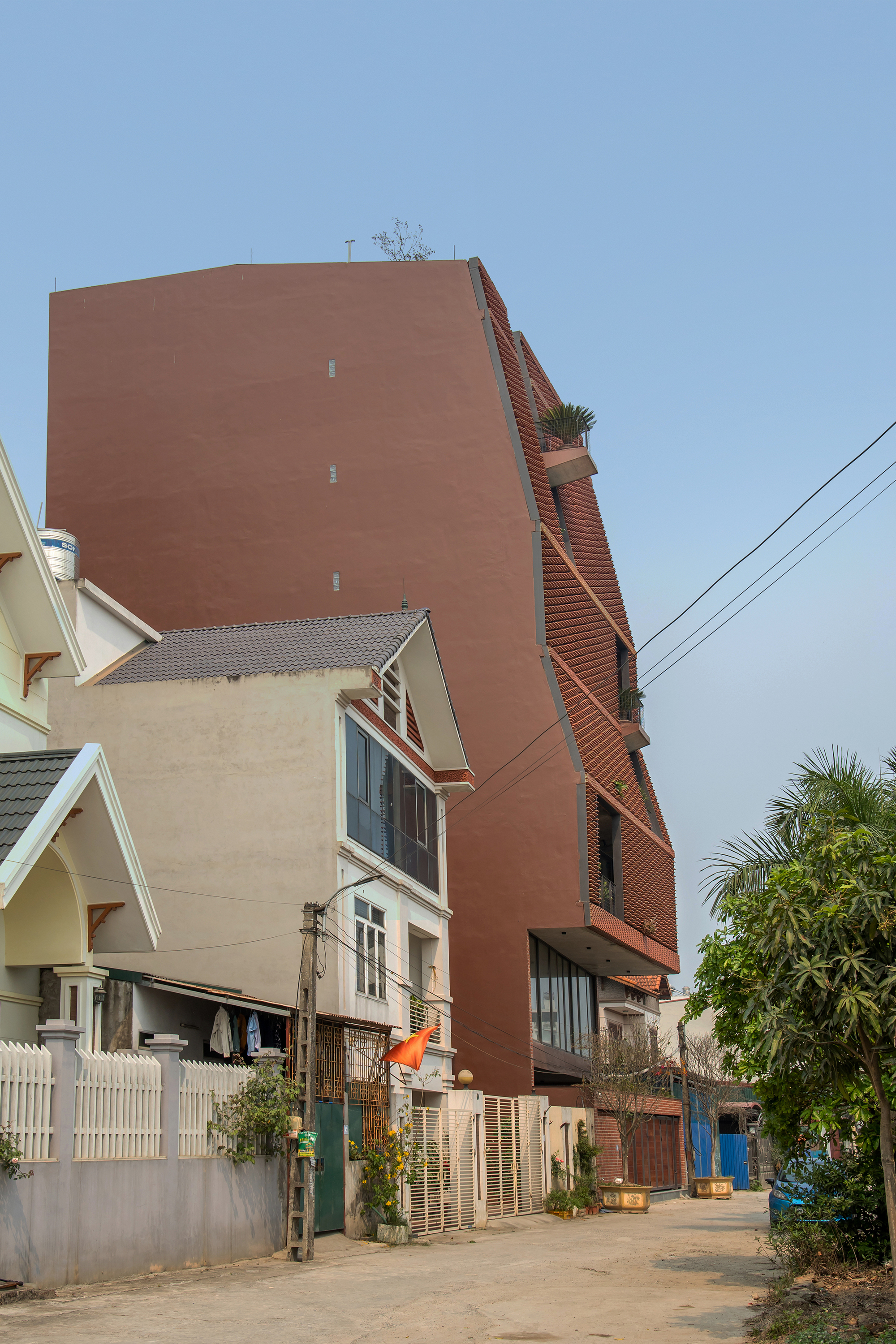 Terracotta brick tower rising above low residential houses along a narrow street with overhead power lines