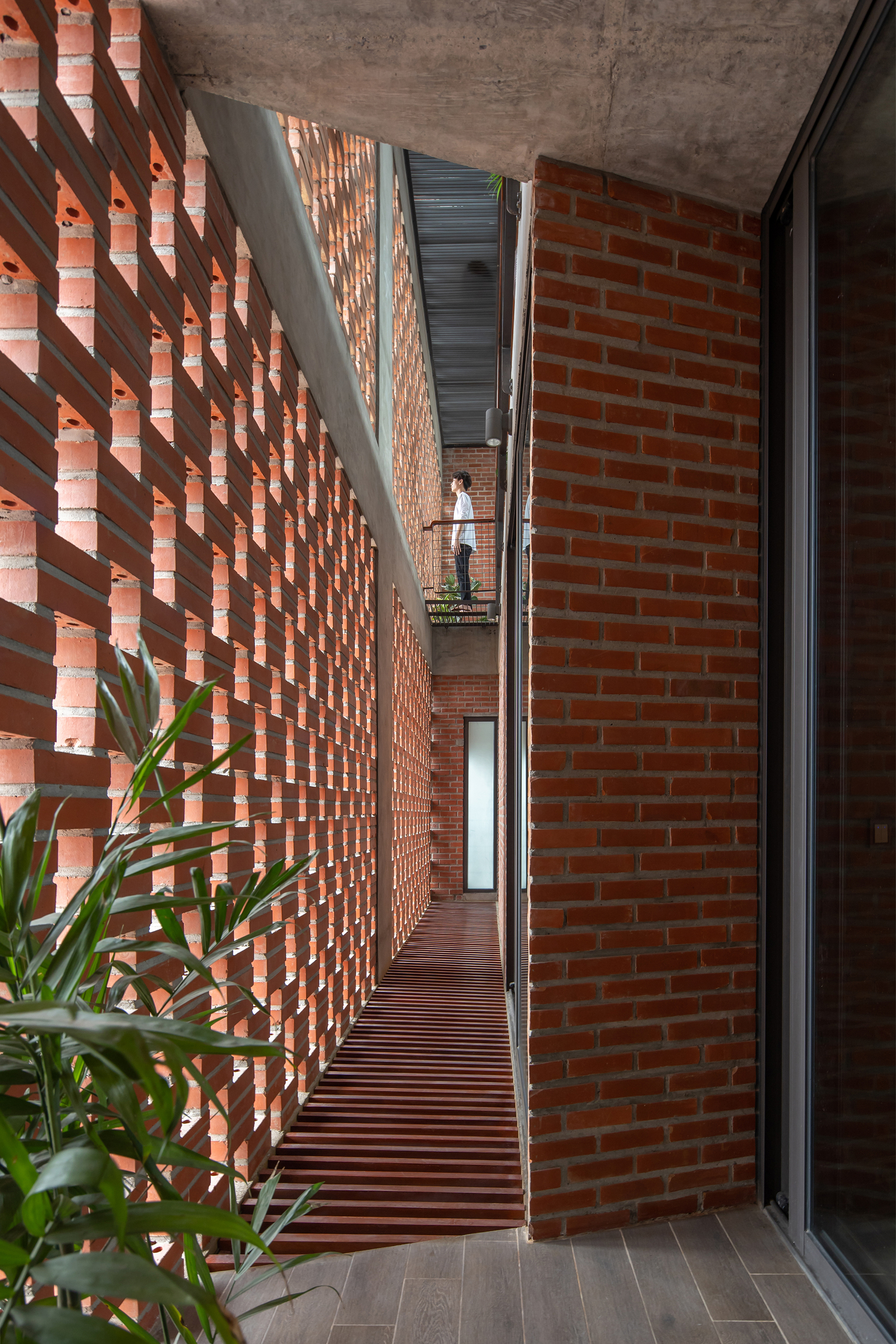 Narrow balcony corridor with open brick screen casting light patterns on the concrete ceiling and floor