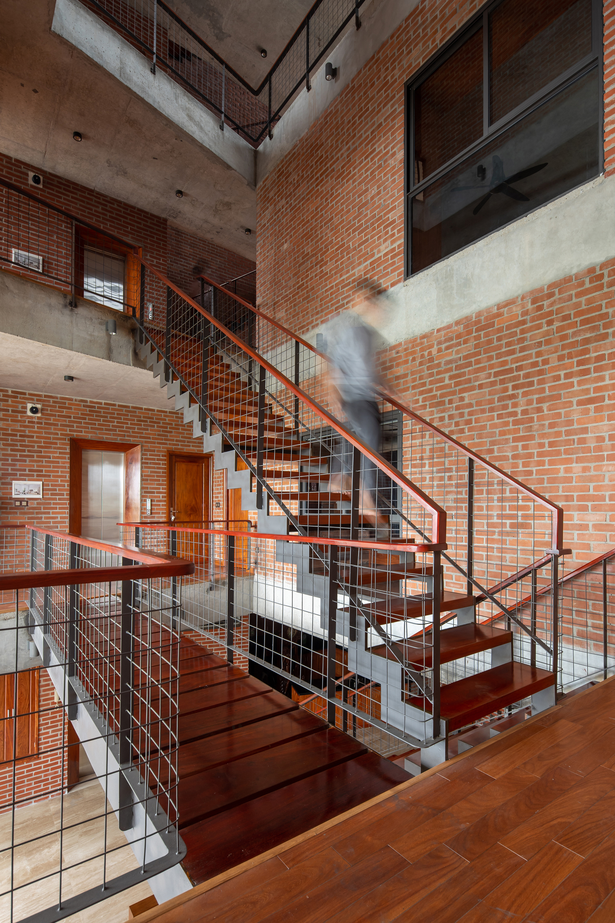 Central staircase with timber treads and mesh railings as a resident descends between brick-walled levels