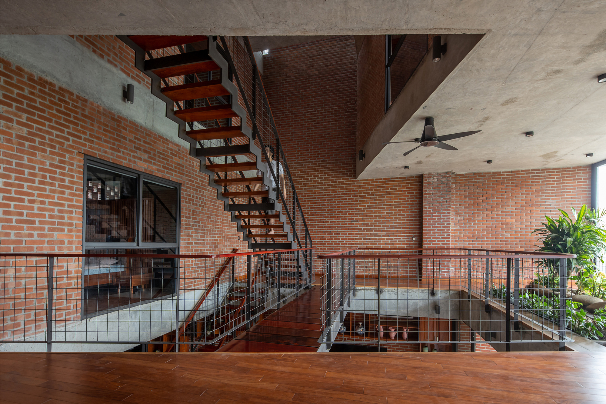 Open-tread timber staircase spanning across a glass-railed balcony with planters beside herringbone wood flooring