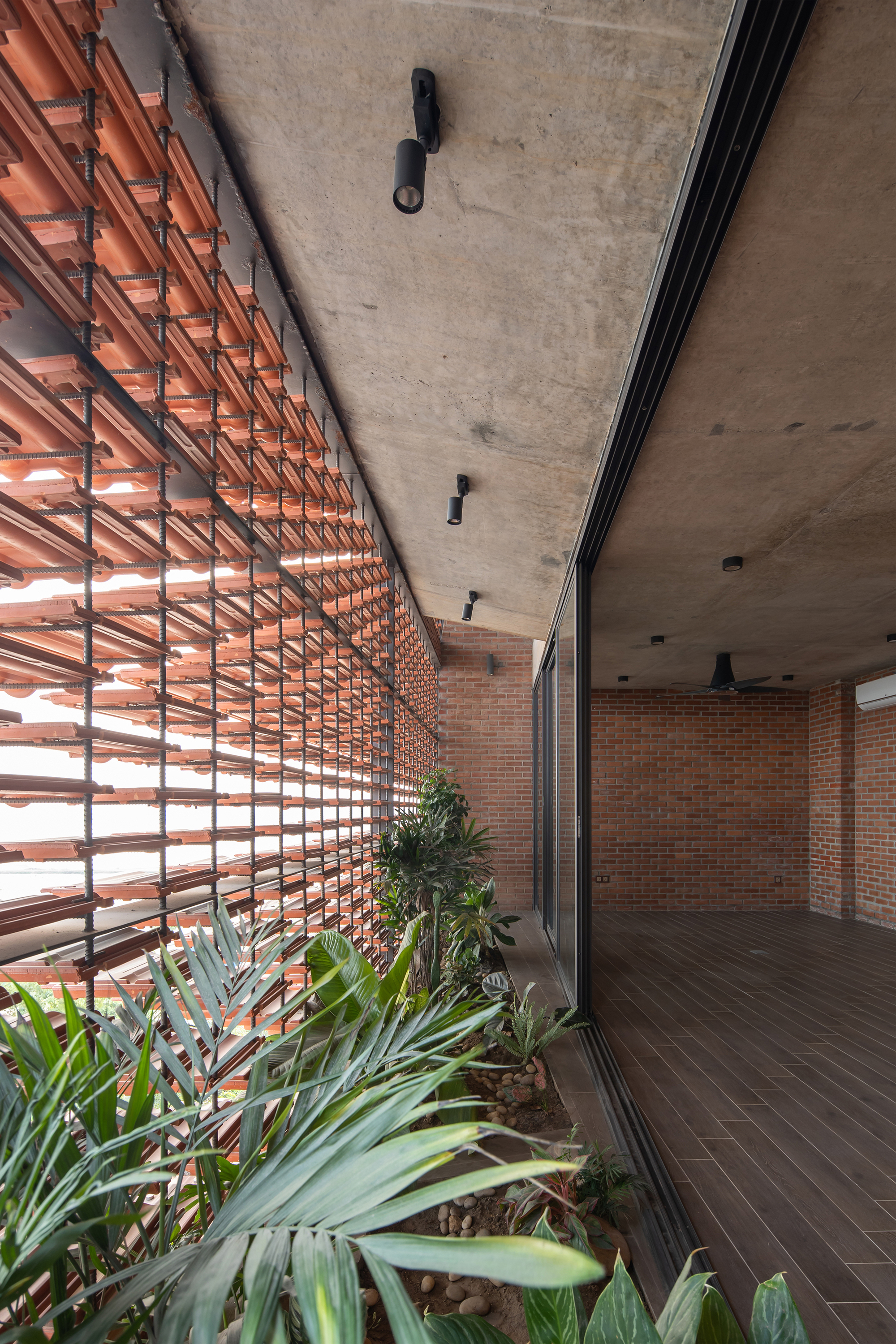 Covered terrace with horizontal terra-cotta louvers filtering daylight over a planted bed with succulents