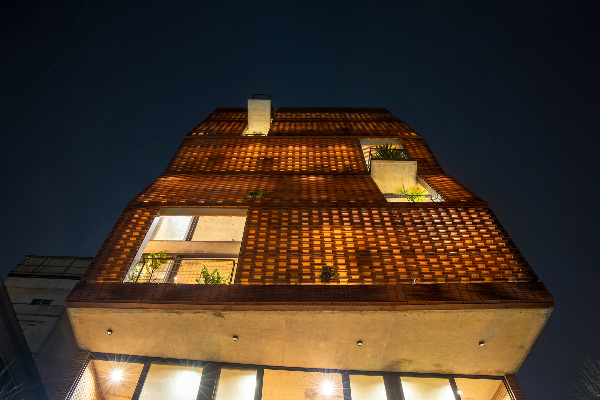 Upward view of the tapered brick facade with glazed openings at night under a dark blue sky