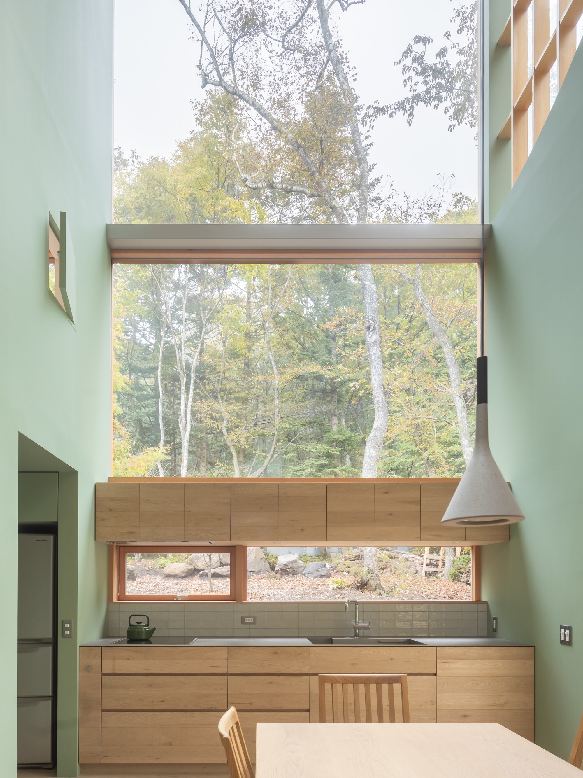 Kitchen with stacked windows framing birch trees and timber cabinetry beneath mint green walls