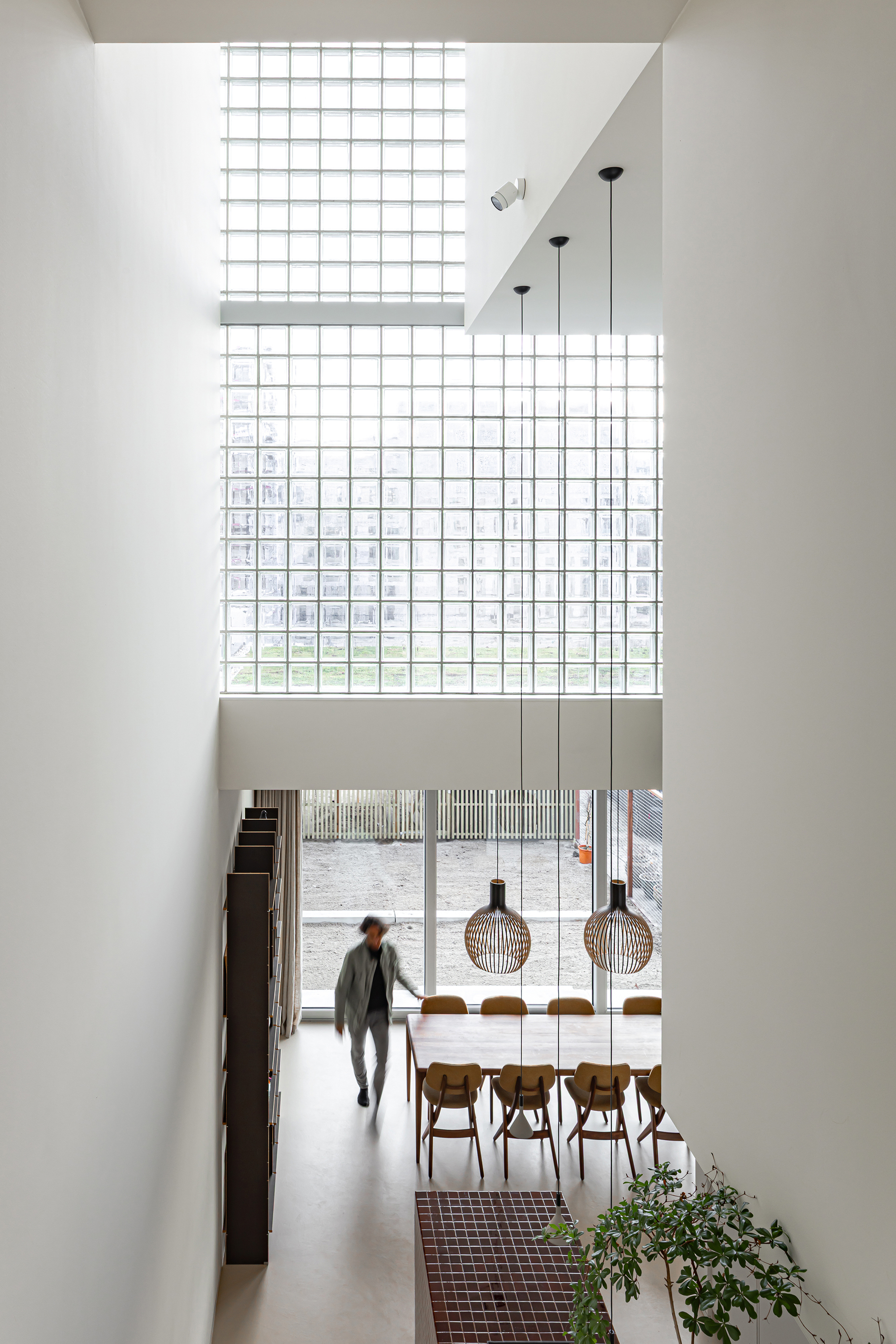 View from upper level showing dining area with pendant lights, glass block clerestory and person walking