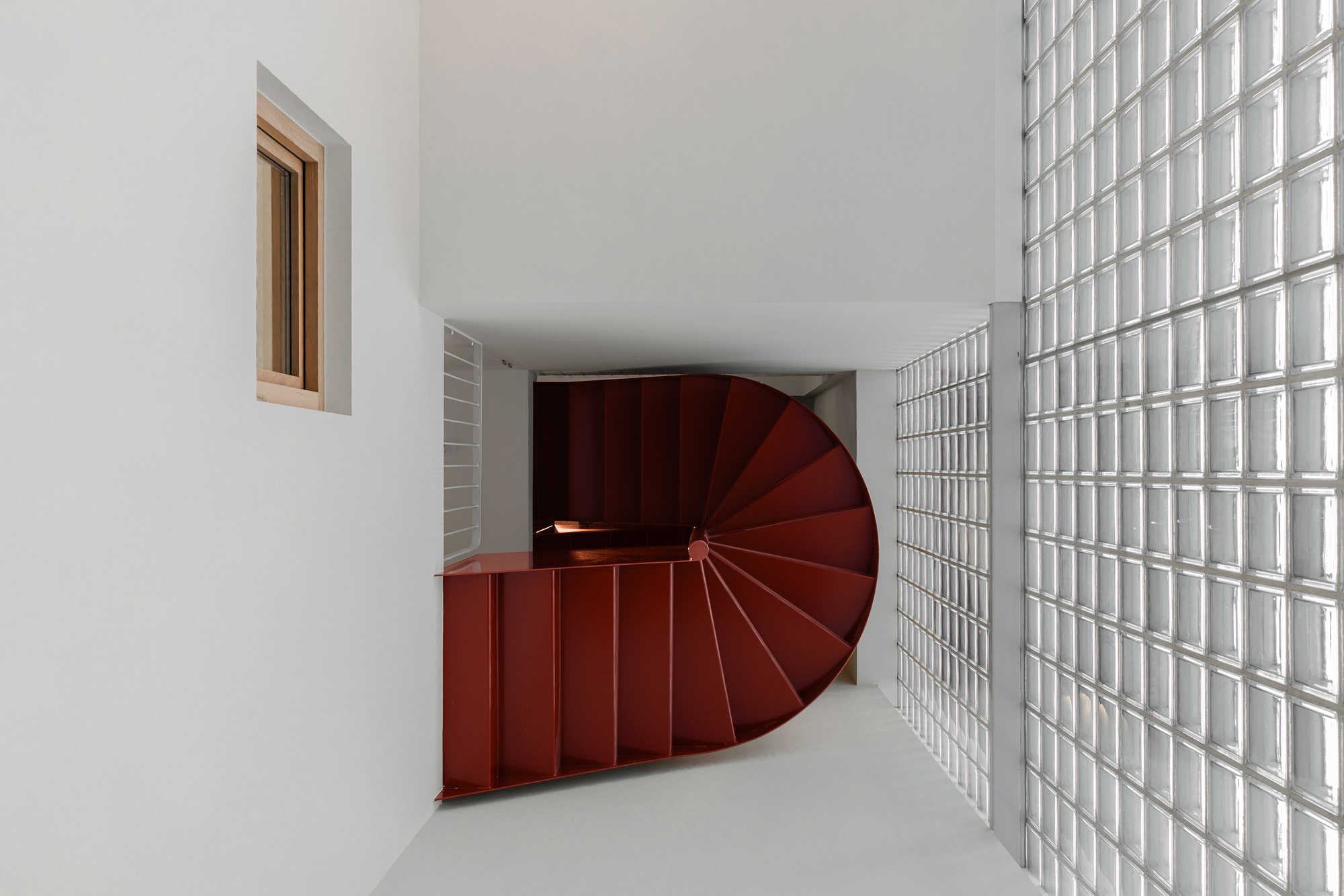 Top view of maroon spiral stair flanked by white glass block wall under curved soffit