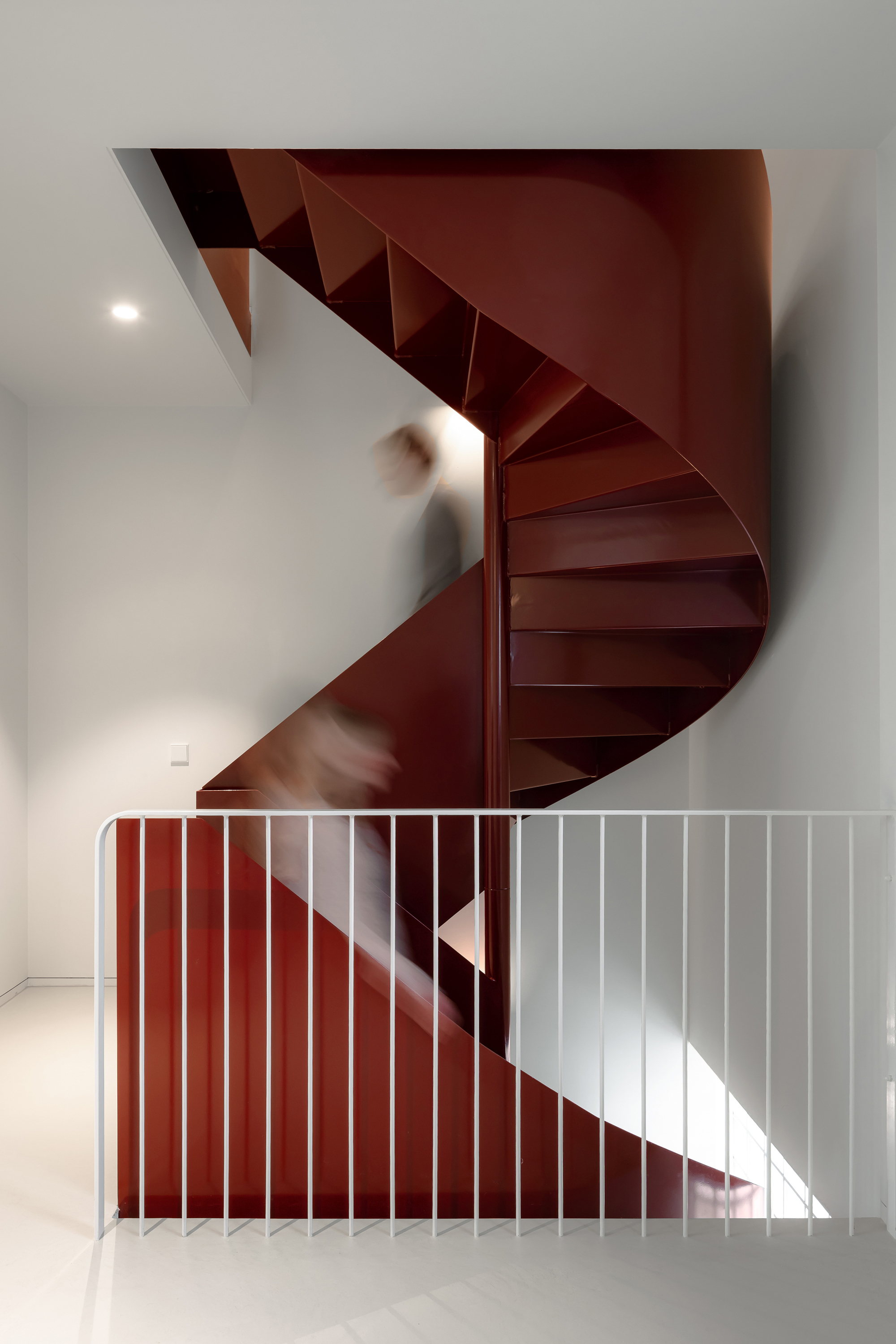 Maroon spiral stair with vertical slat balustrade and person in motion ascending the treads