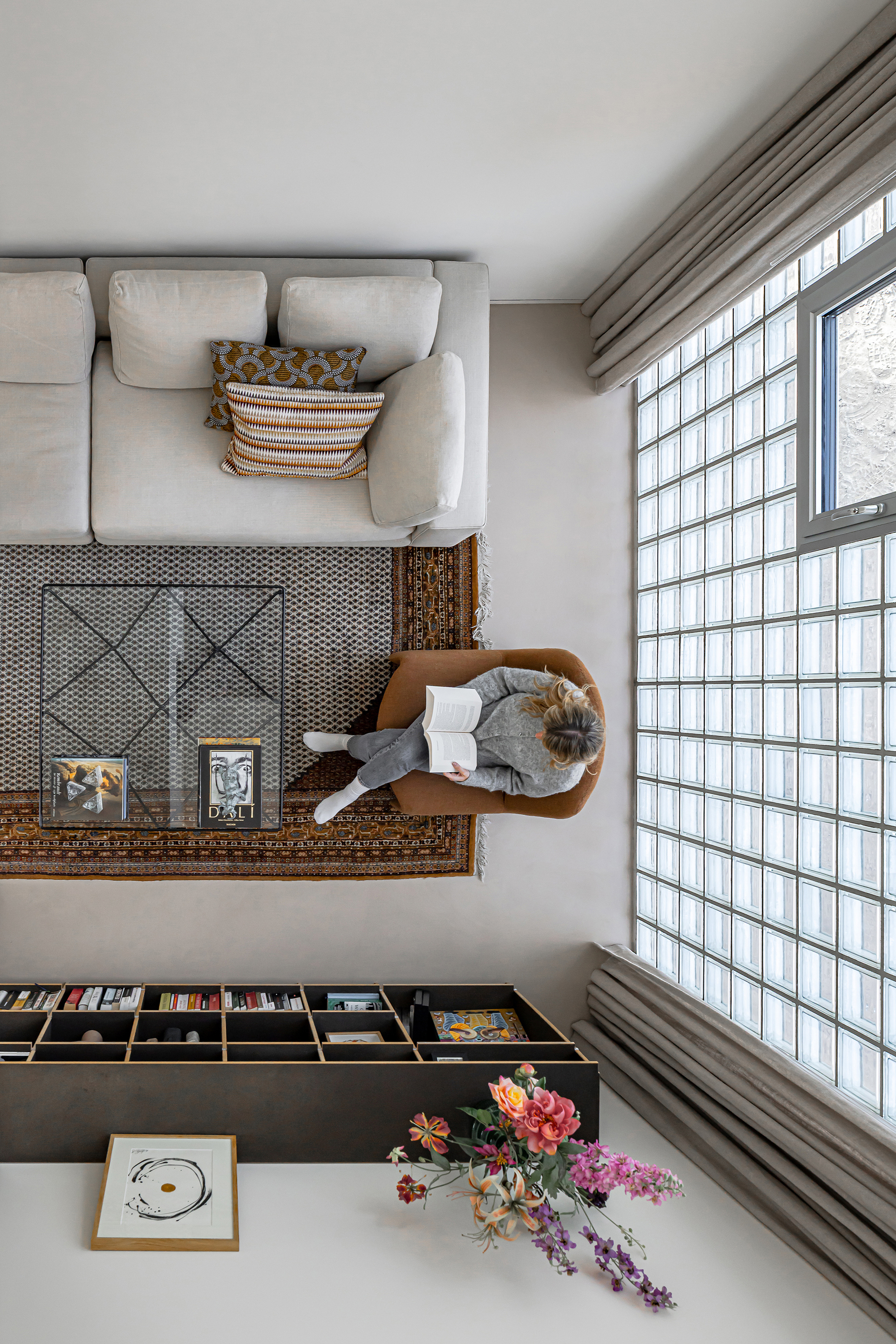 Top-down view of a living room with glass block wall, cream sofa, and person sitting on a rug