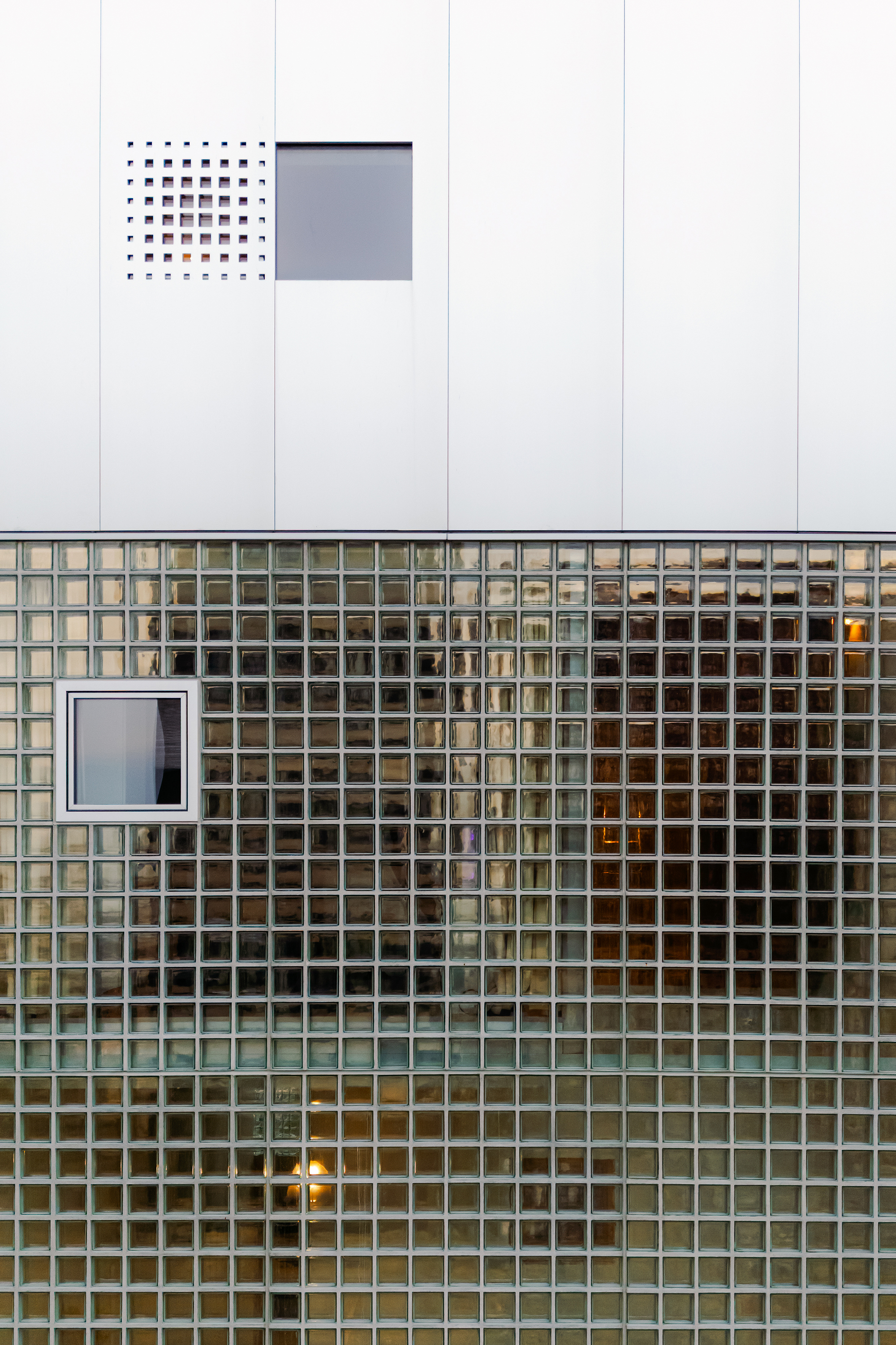 White paneled wall with perforated vent above glass block strip with embedded window