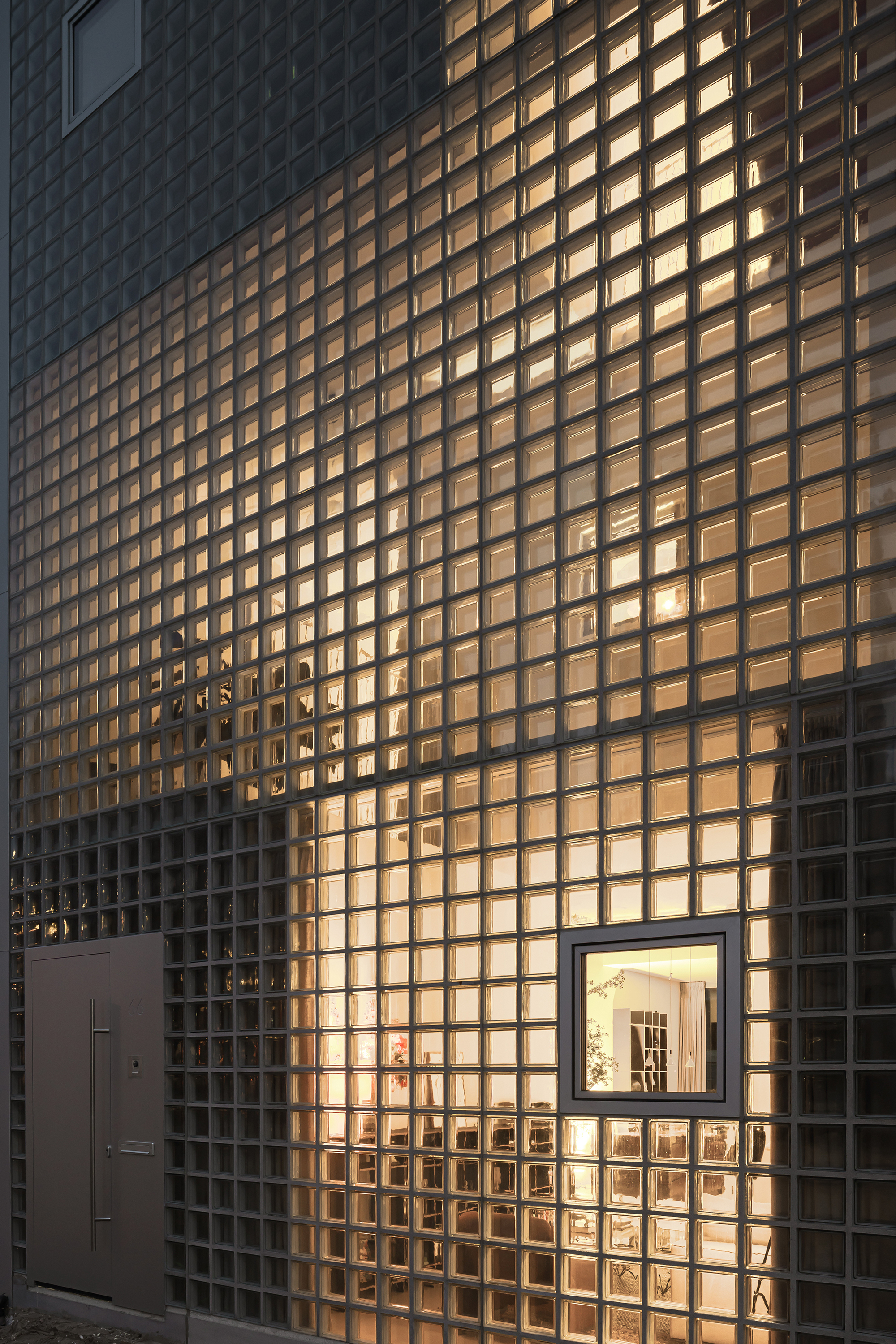 Glass block facade illuminated from within at dusk with a framed window opening