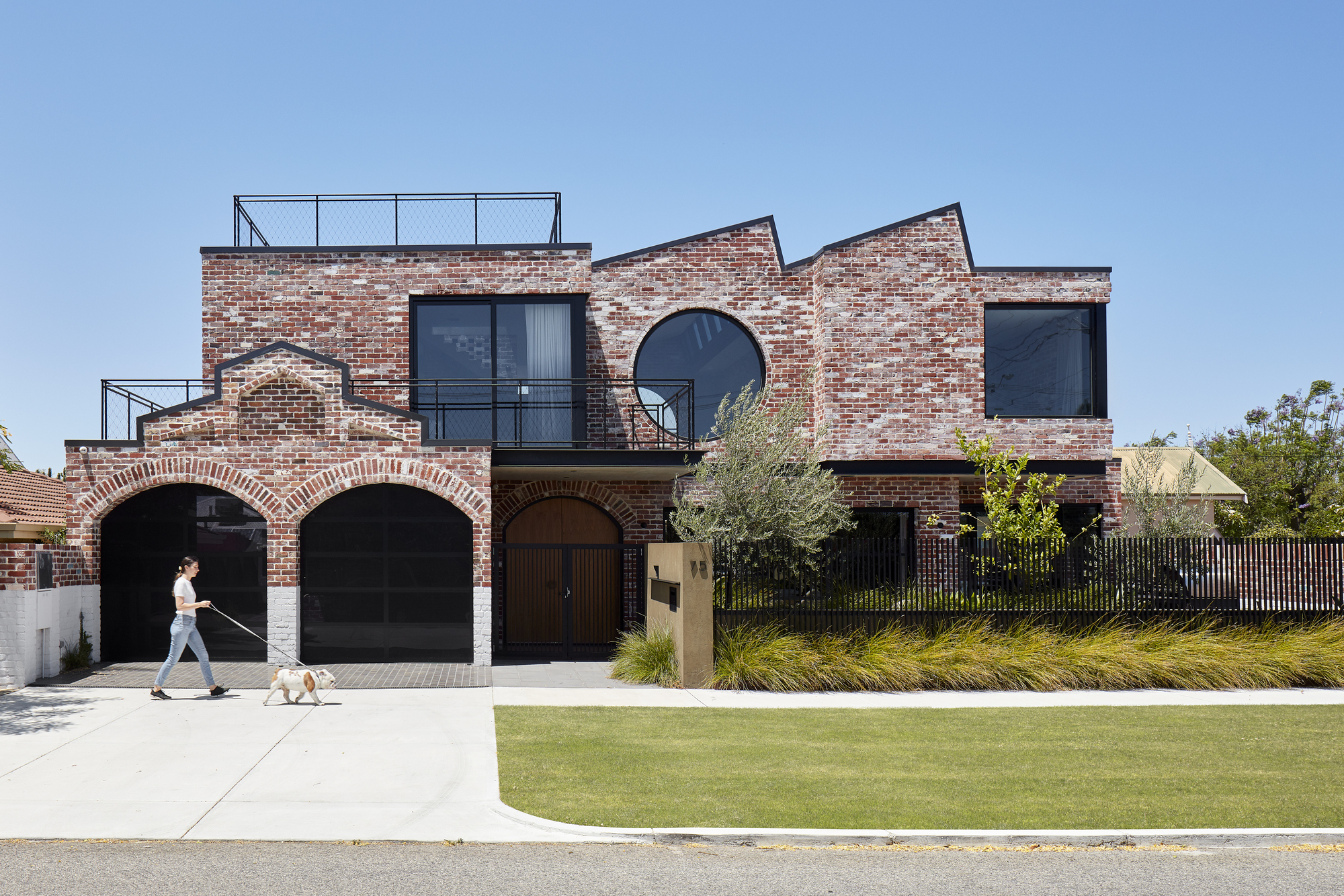 Street view of the red brick facade with arched openings and a person walking a dog