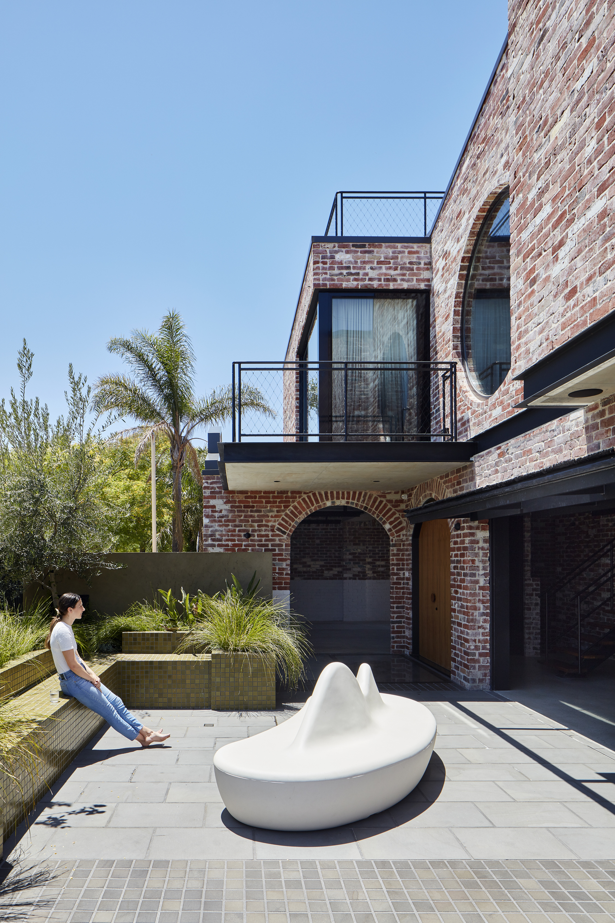 Courtyard with white sculptural seating and a woman sitting on the concrete planter edge