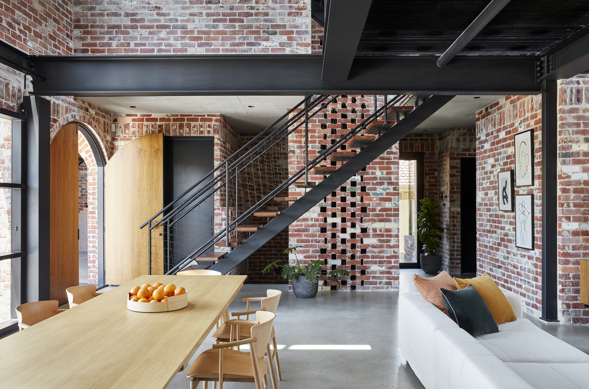 Living space with exposed brick walls and black steel staircase ascending beneath structural beams