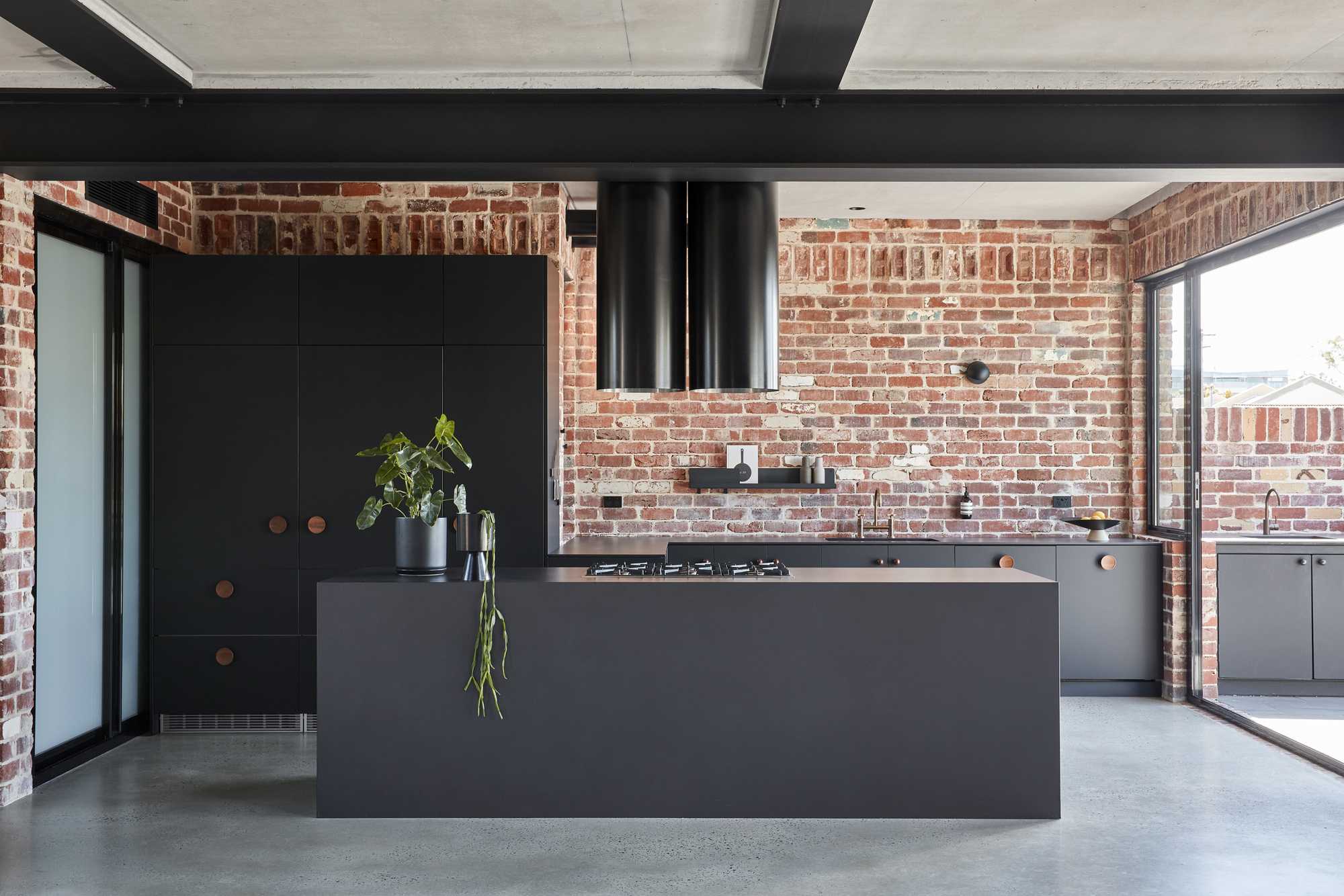 Black matte kitchen island beneath exposed brick walls and a cylindrical range hood
