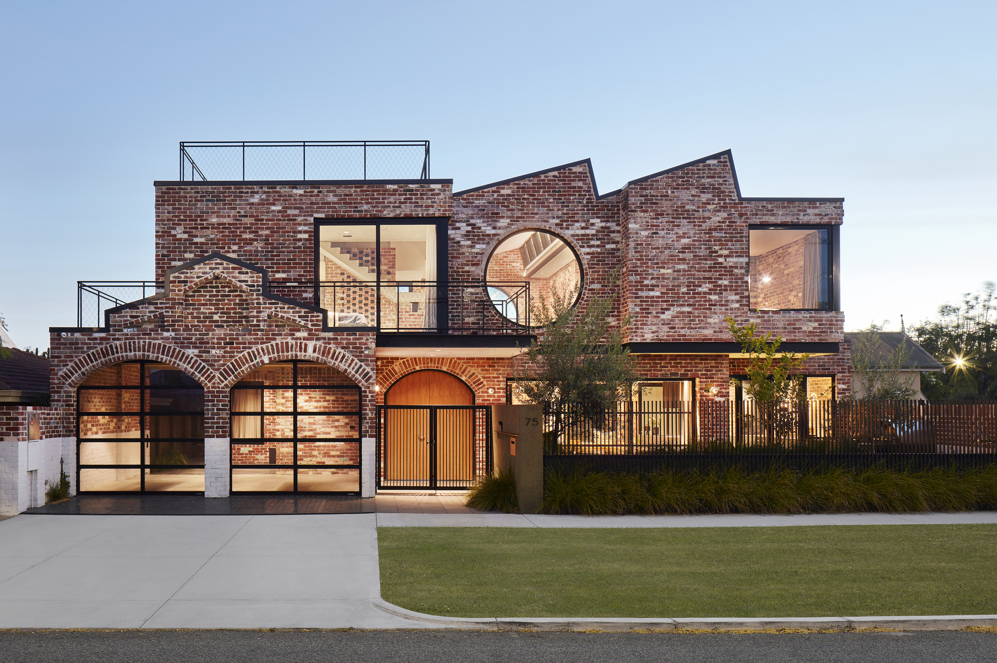 Street facade with brick arches framing garage doors and a circular window at dusk