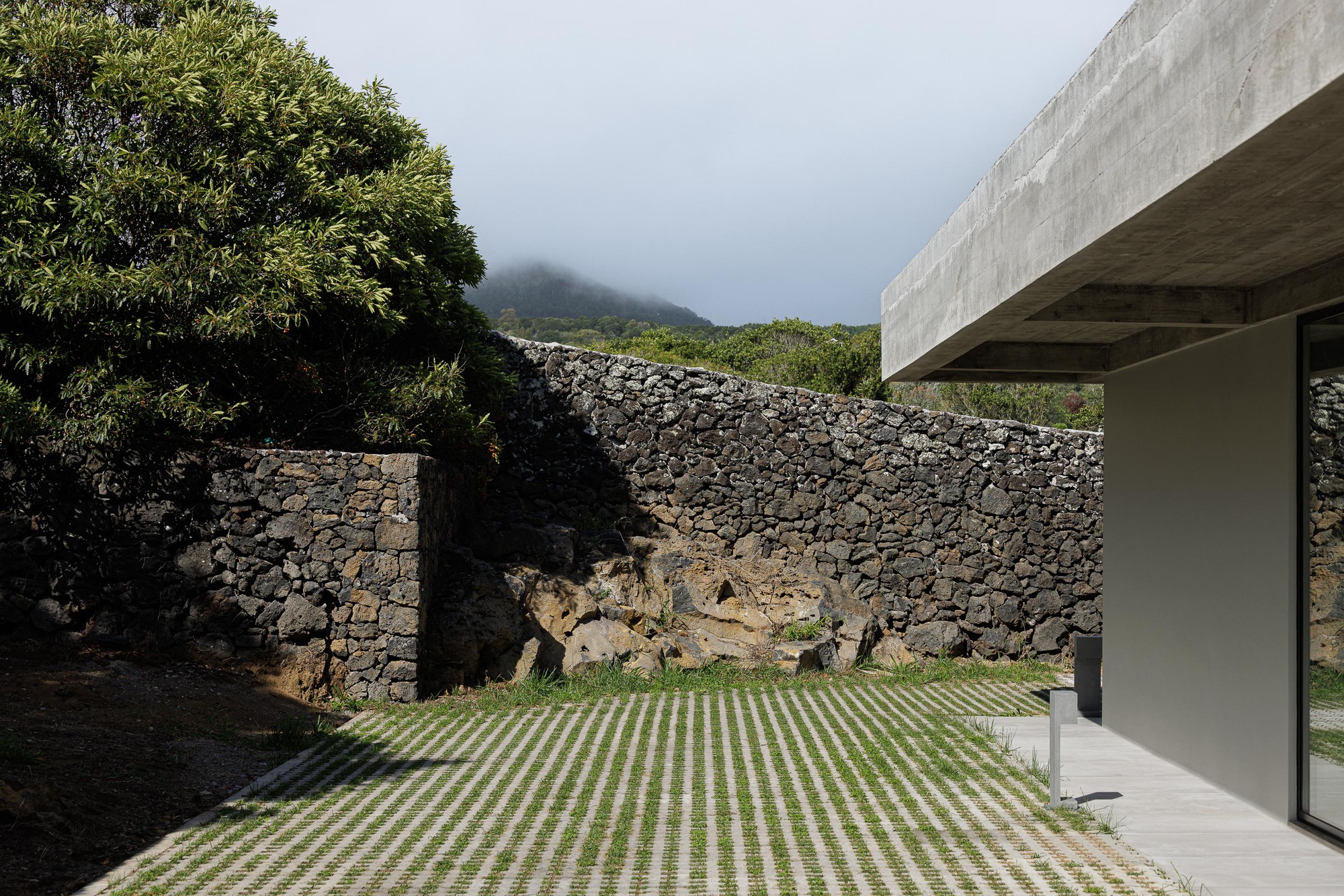 Courtyard with grid-patterned paving and volcanic stone walls against a mist-covered hillside